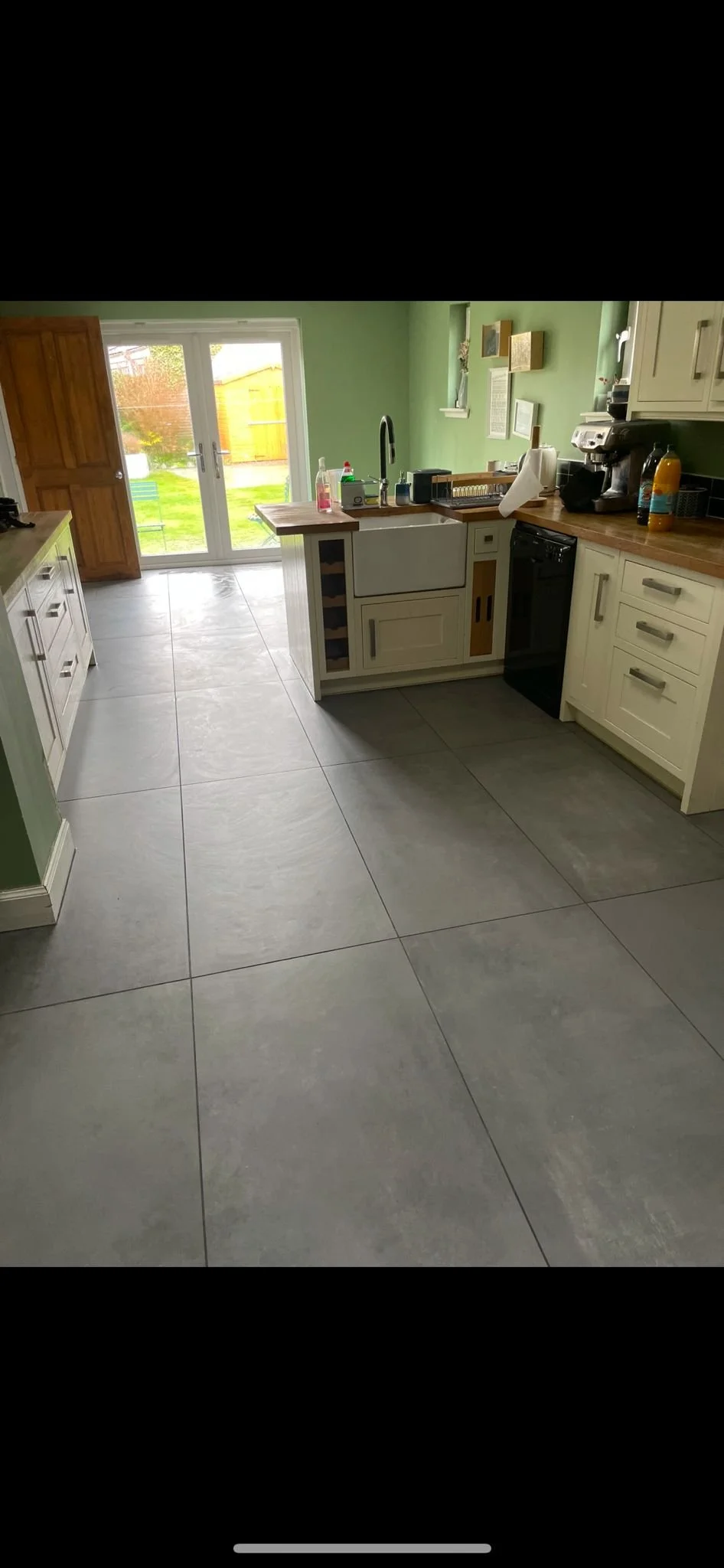 Kitchen with green walls, large tiled floor, wooden door and sliding glass doors leading outside, white cabinets, countertop with various appliances, and a small kitchen island.