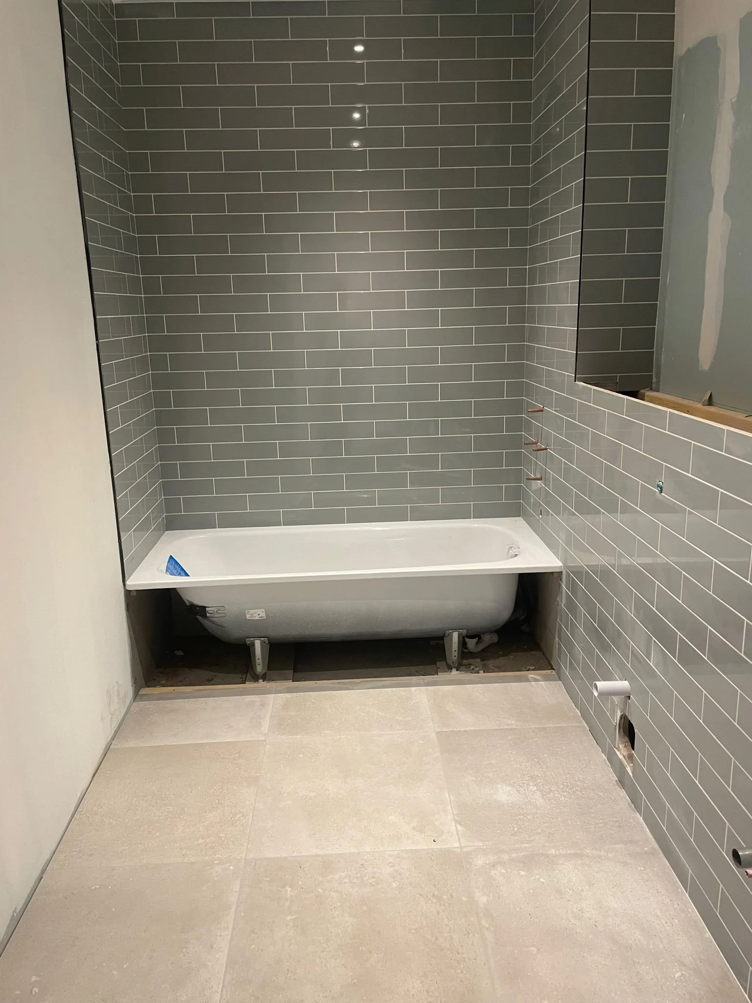 Bathroom under construction with a partially installed bathtub, gray subway tile walls, and light beige tile flooring.