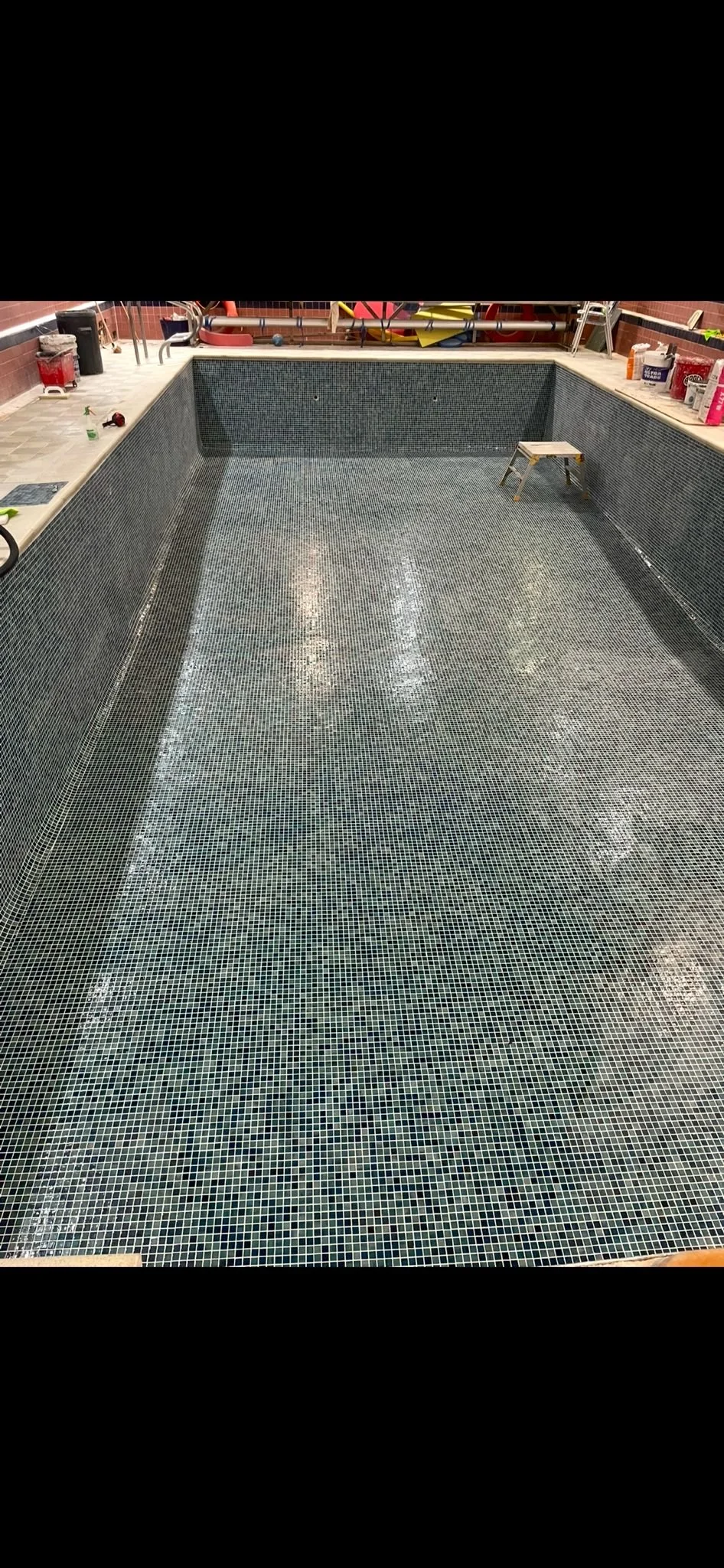 Empty swimming pool with small mosaic tiles and cleaning tools around.