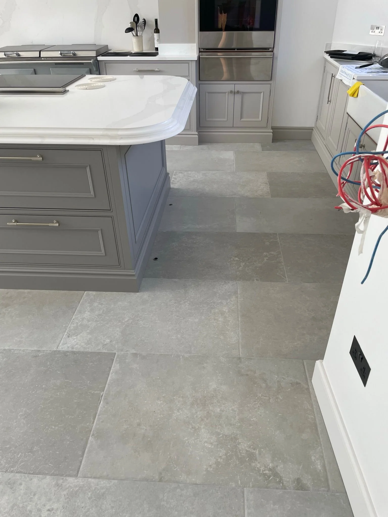 Kitchen with gray cabinets, a white marble island, and large gray tile flooring. Some electrical wiring is visible on the right side.