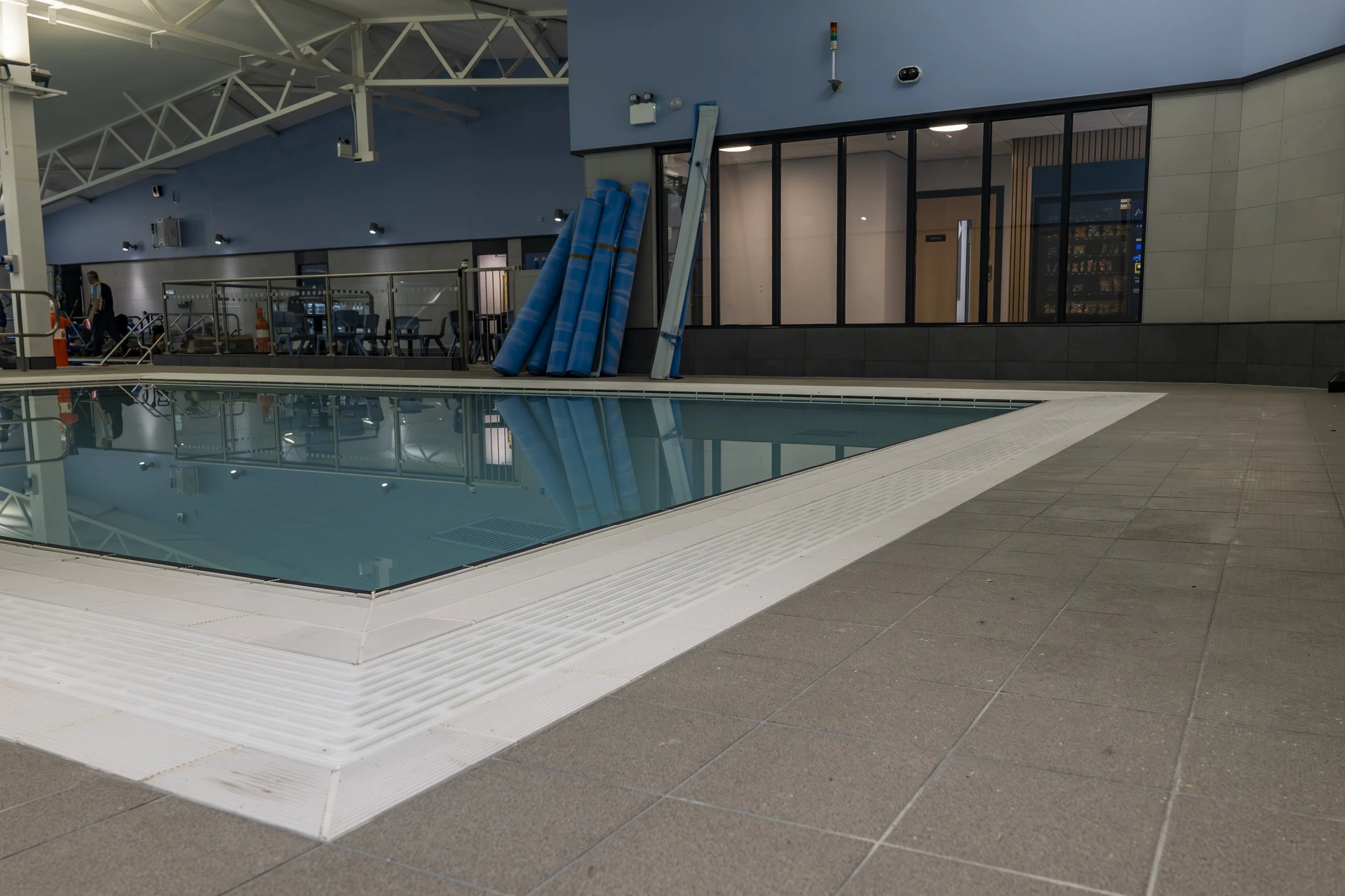 Indoor swimming pool area with a pool, pool accessories, and a lounge area behind glass walls.