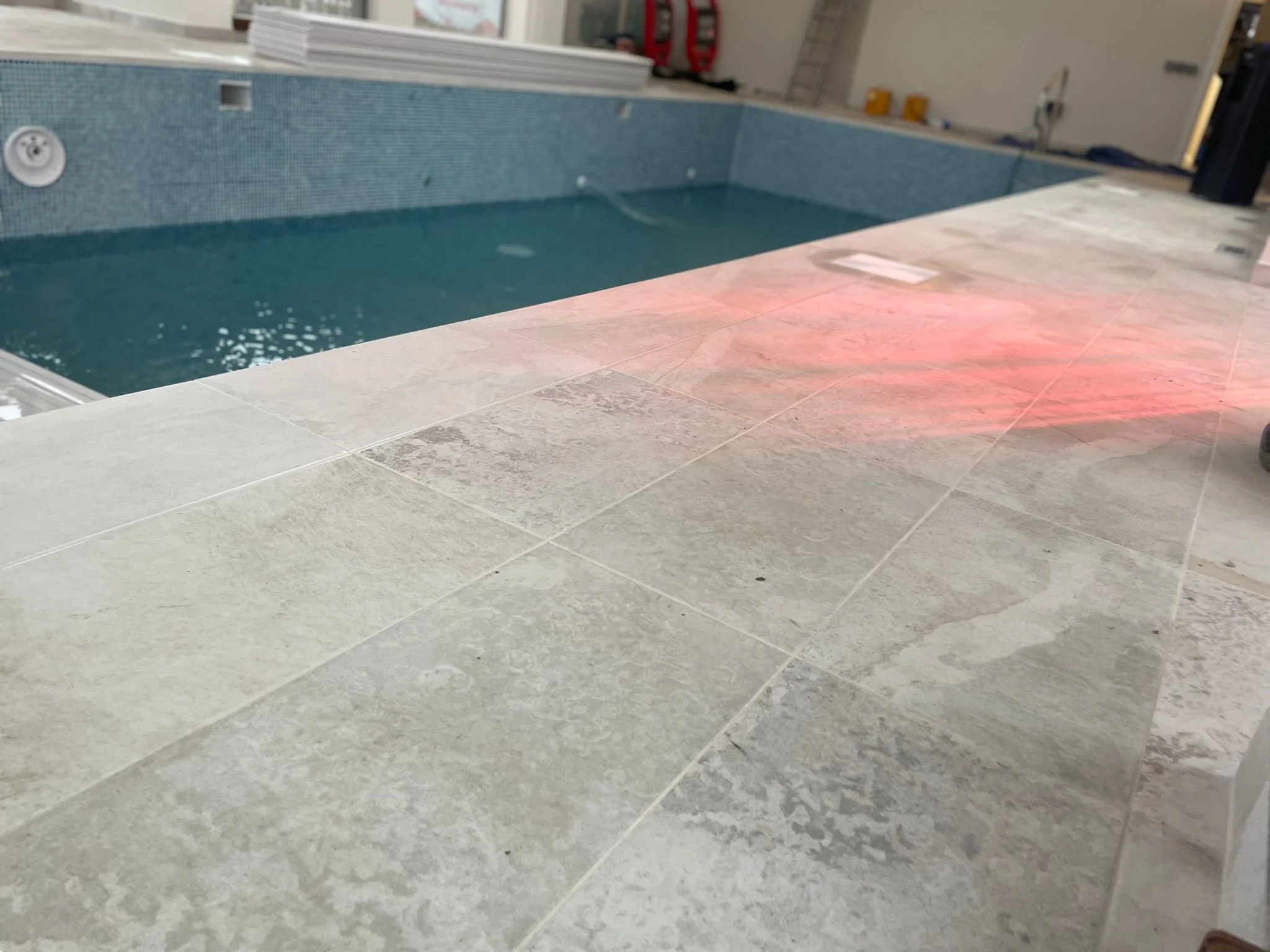 Construction site with tiled surface and an empty swimming pool in the background.