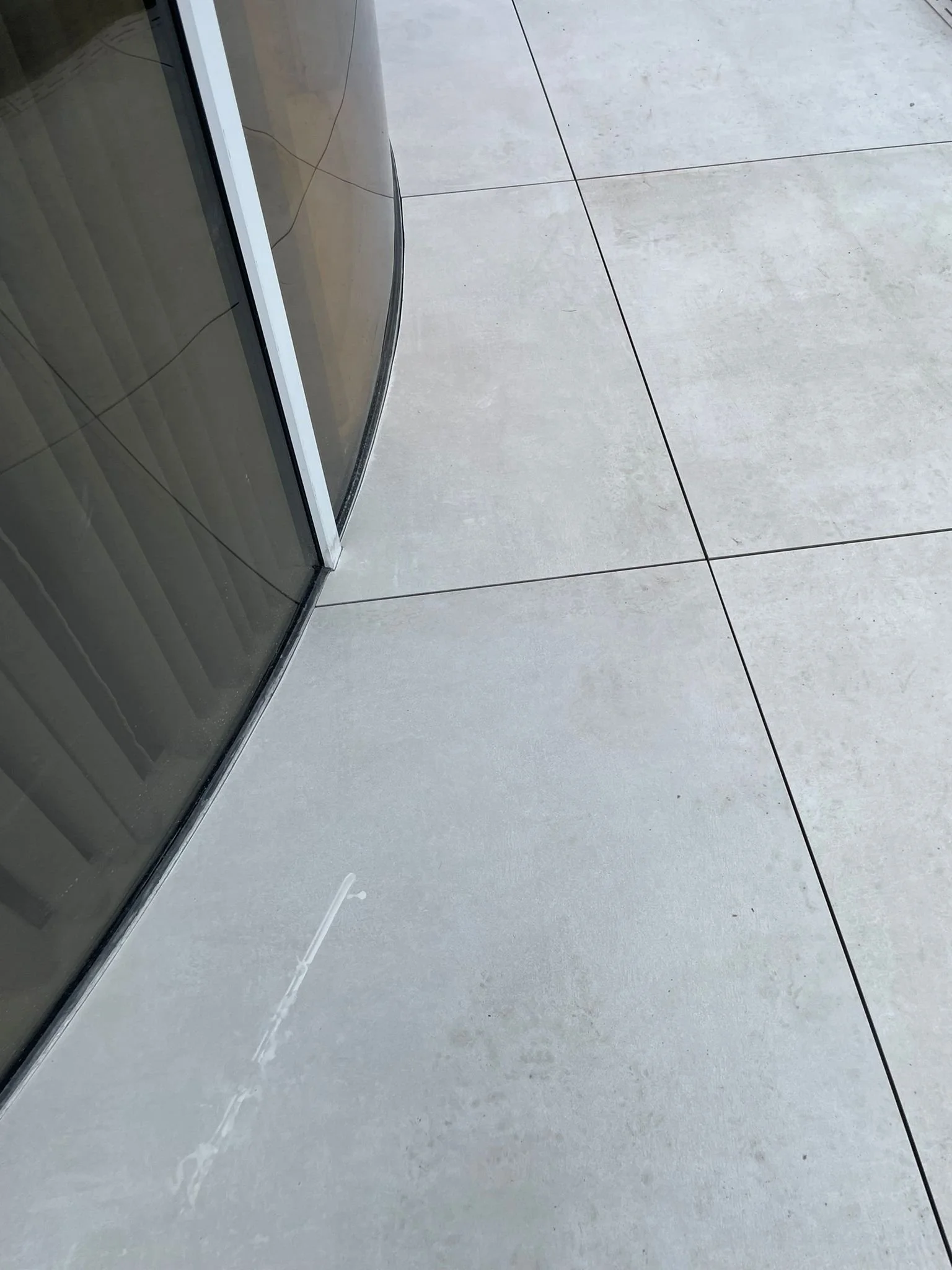 Close-up of tiled floor outside glass door with smudge marks and a thin line of scratch or paint residue.