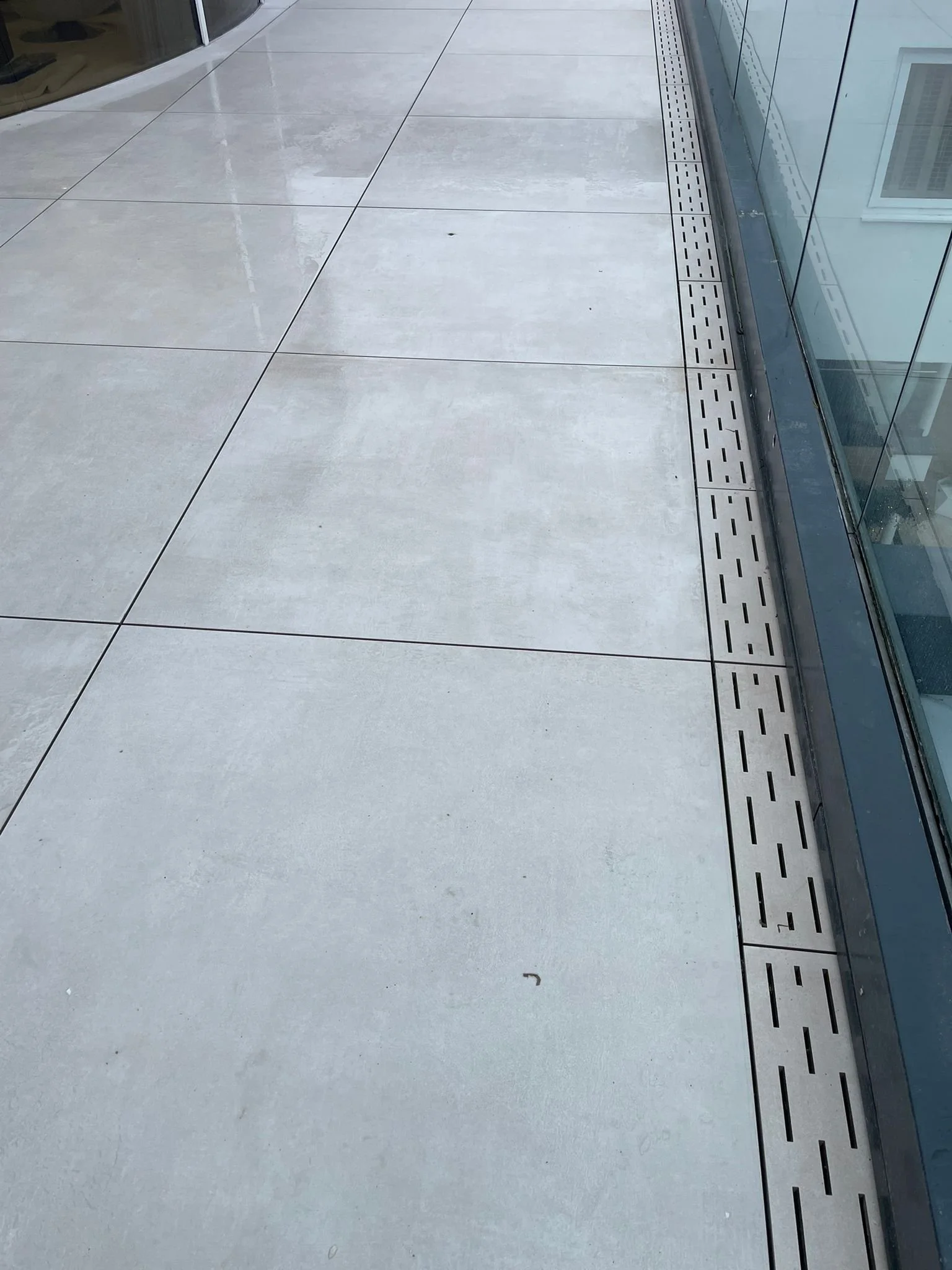 Empty outdoor balcony with large concrete tiles and a glass railing.