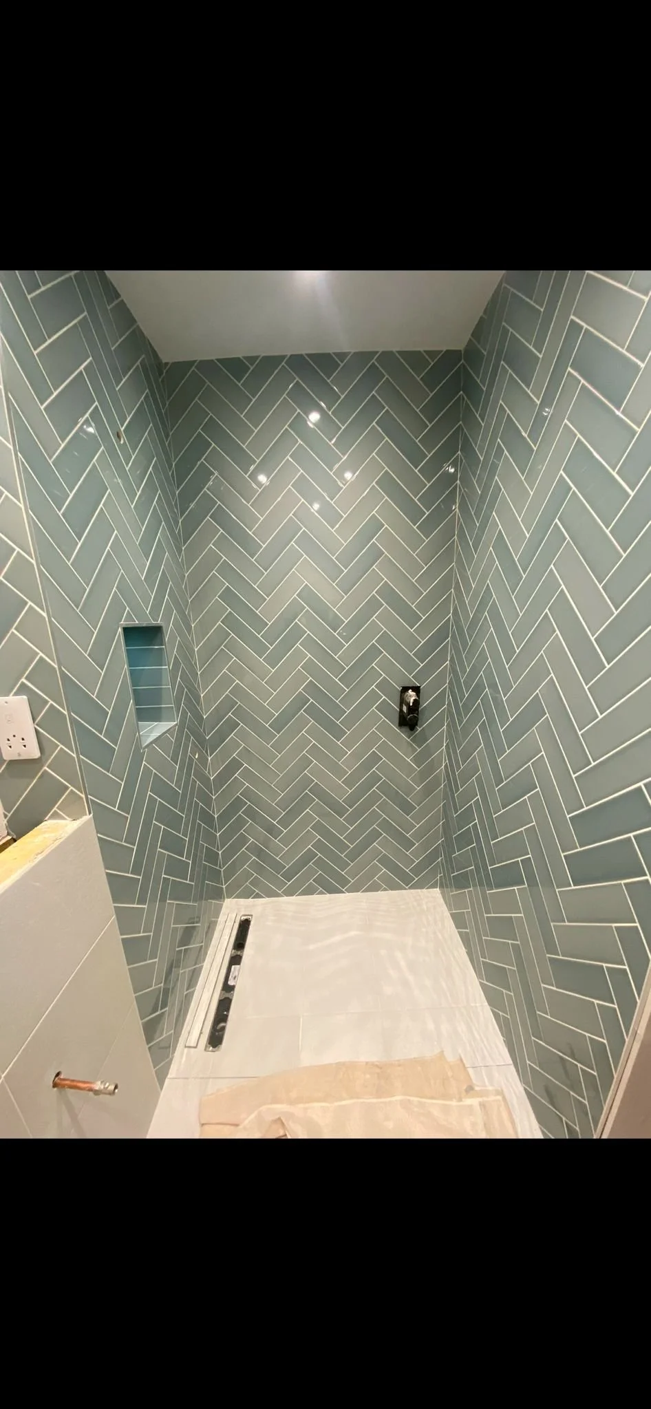 Bathroom with blue herringbone tile walls, unfinished with no fixtures or shower head installed, and a level placed on the floor.