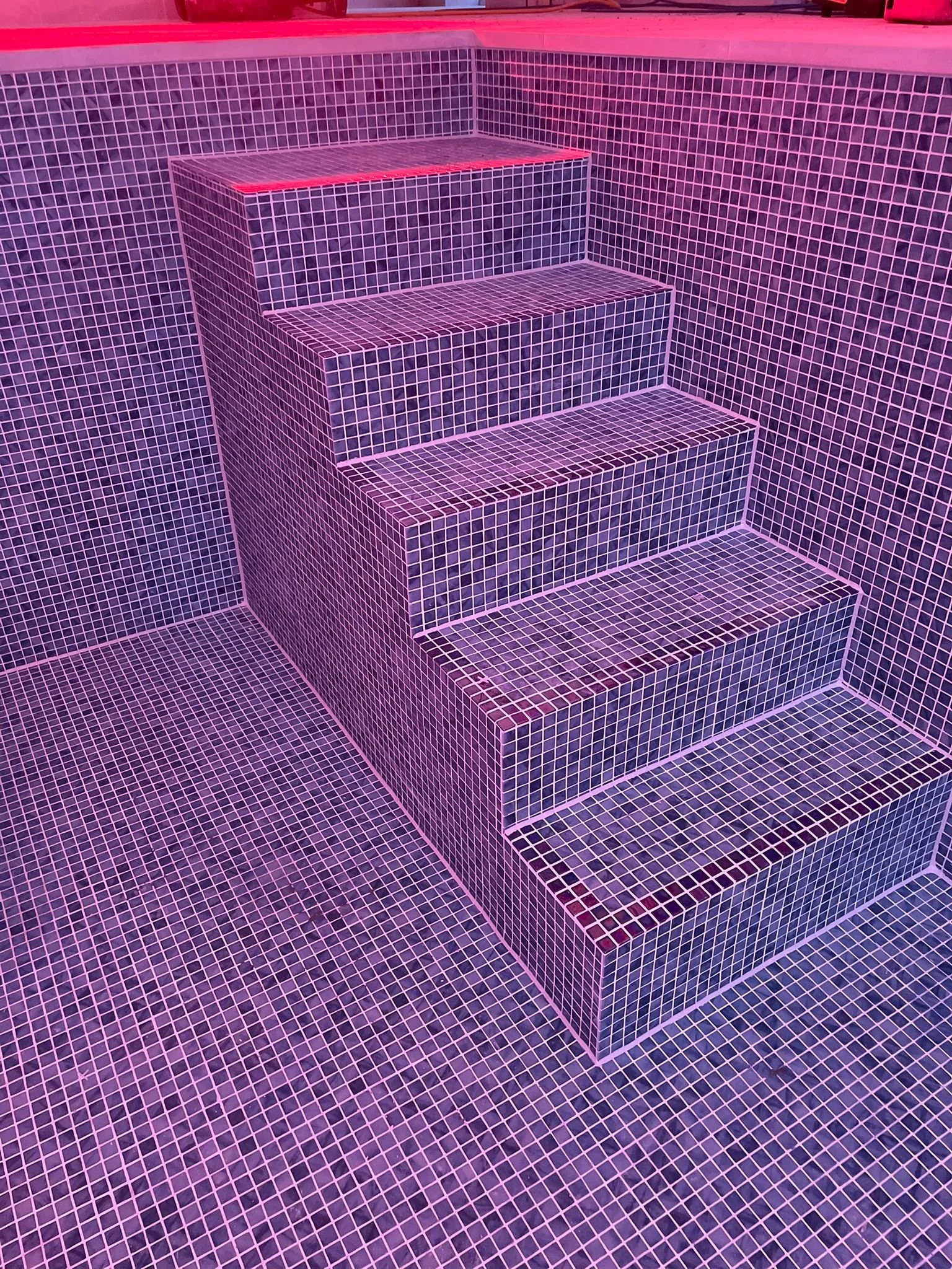 Pink-lit tiled staircase with five steps and tiled walls and floor.