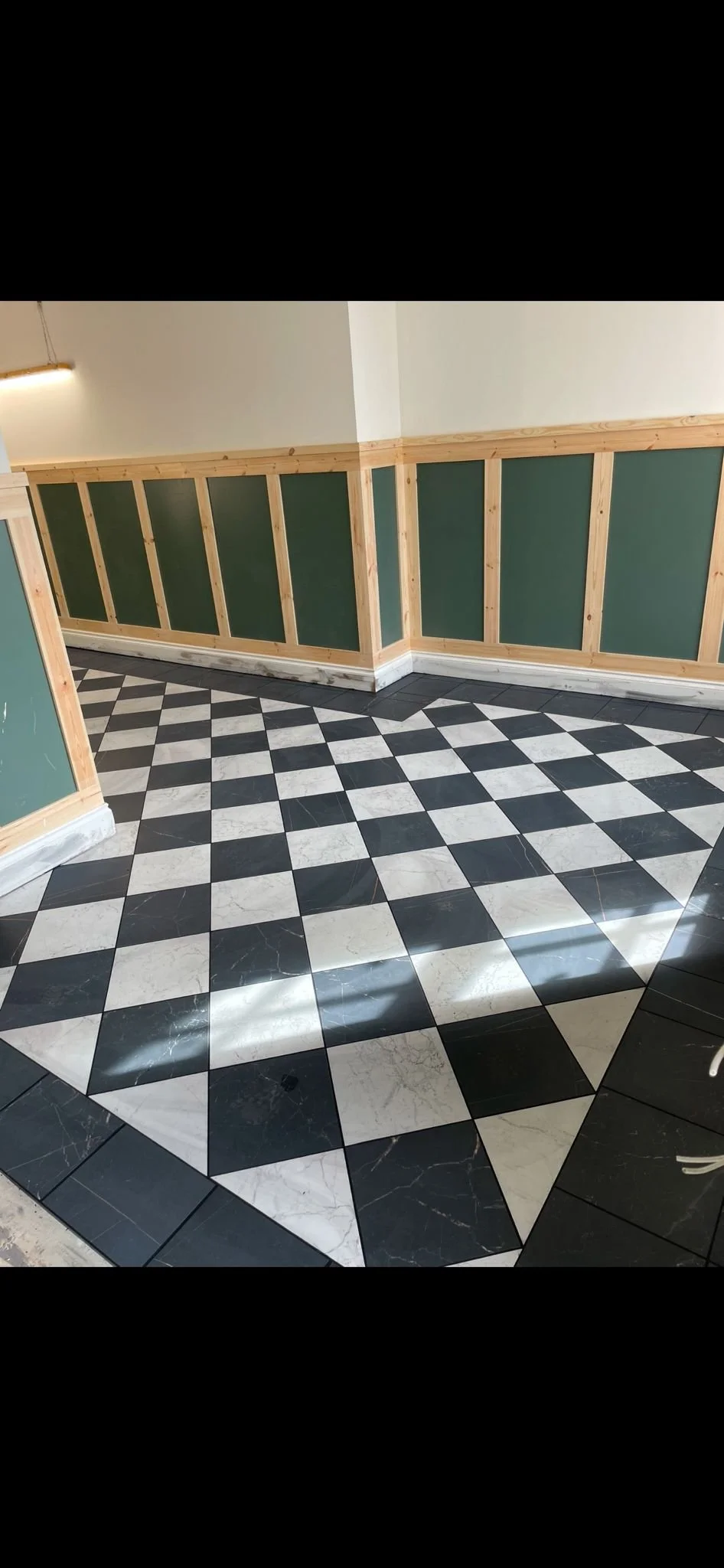 Interior room corner with checkered black and white marble floor tiles and green and wood-paneled walls.