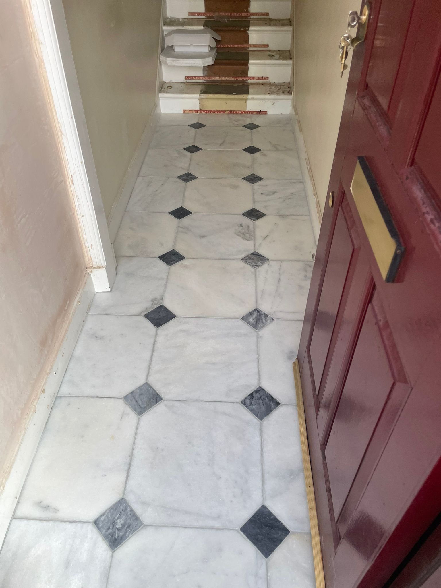 Interior view of a front door with a marble floor and stairs leading up, with some stacked boxes at the top of the stairs.