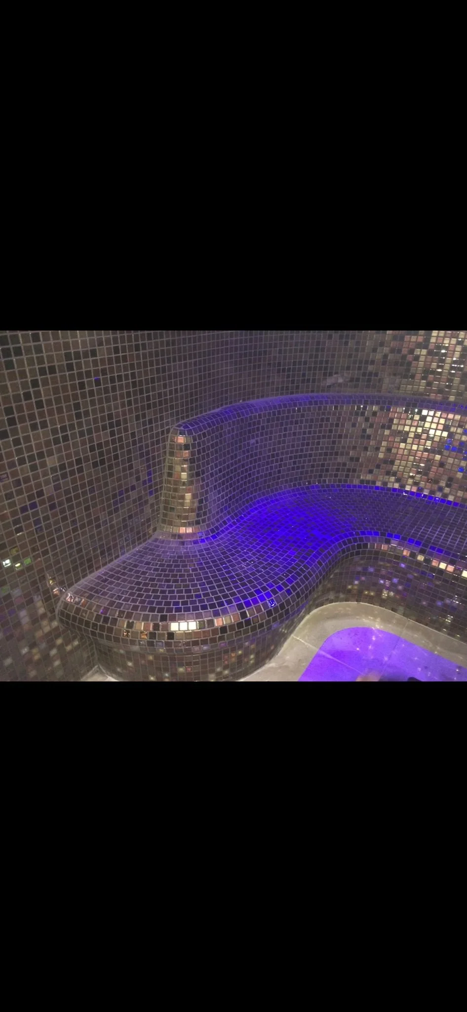 A mosaic tiled curved surface illuminated with purple and blue lighting.