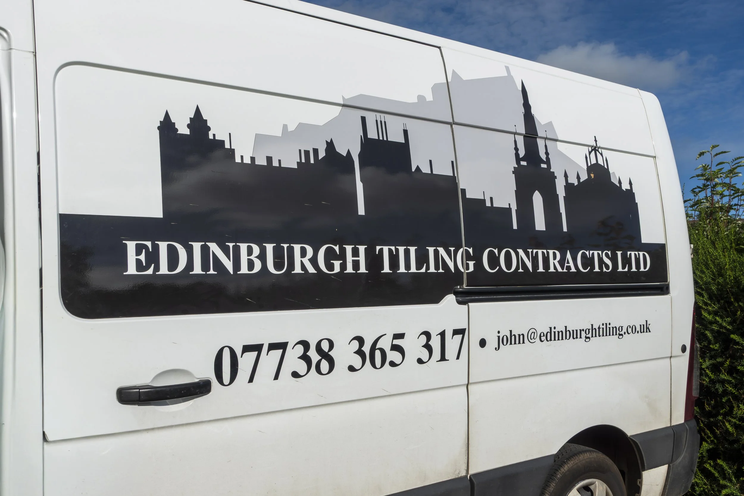 White van with black signage displaying a city skyline silhouette and text promoting Edinburgh Tiling Contracts Ltd, including phone number and email address.