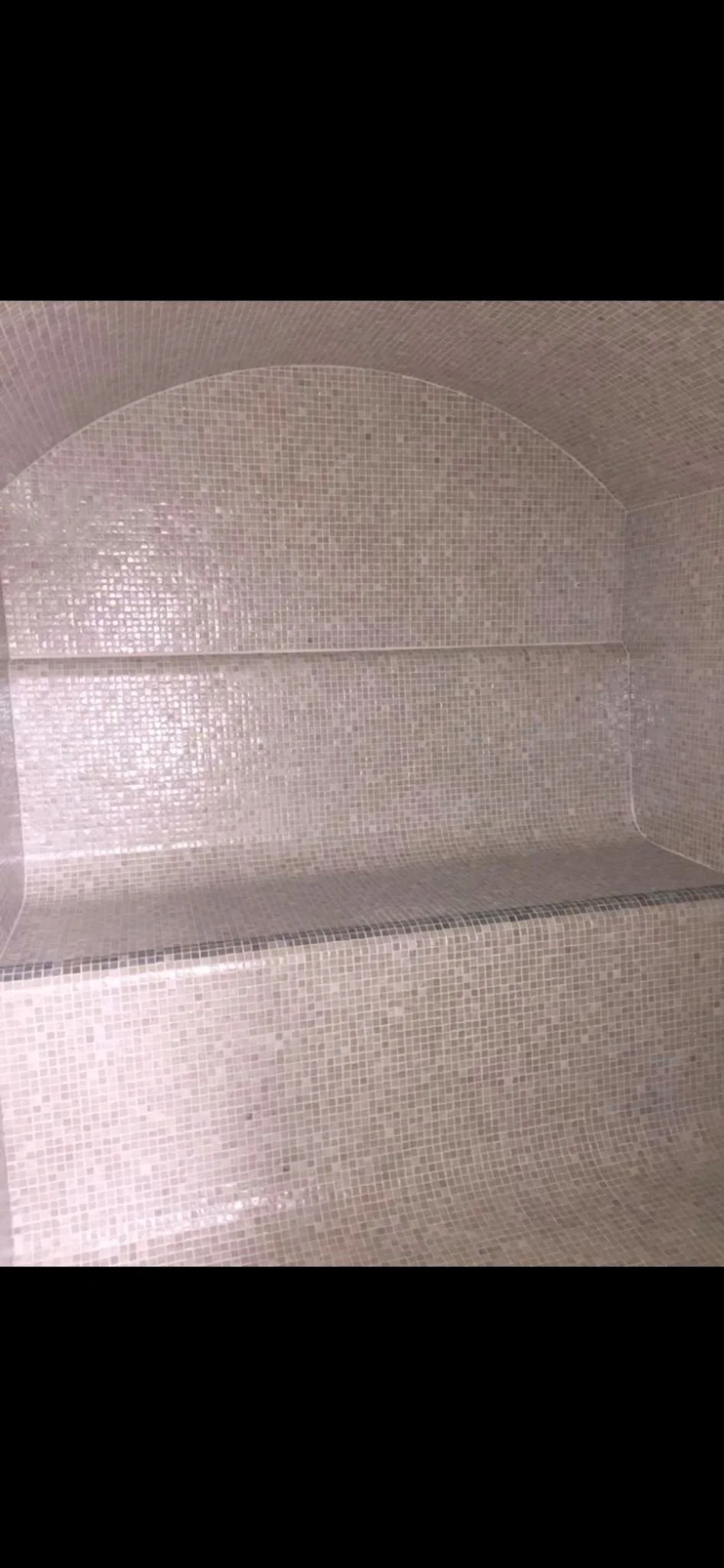 Empty tiled shower with a curved ceiling and a built-in bench