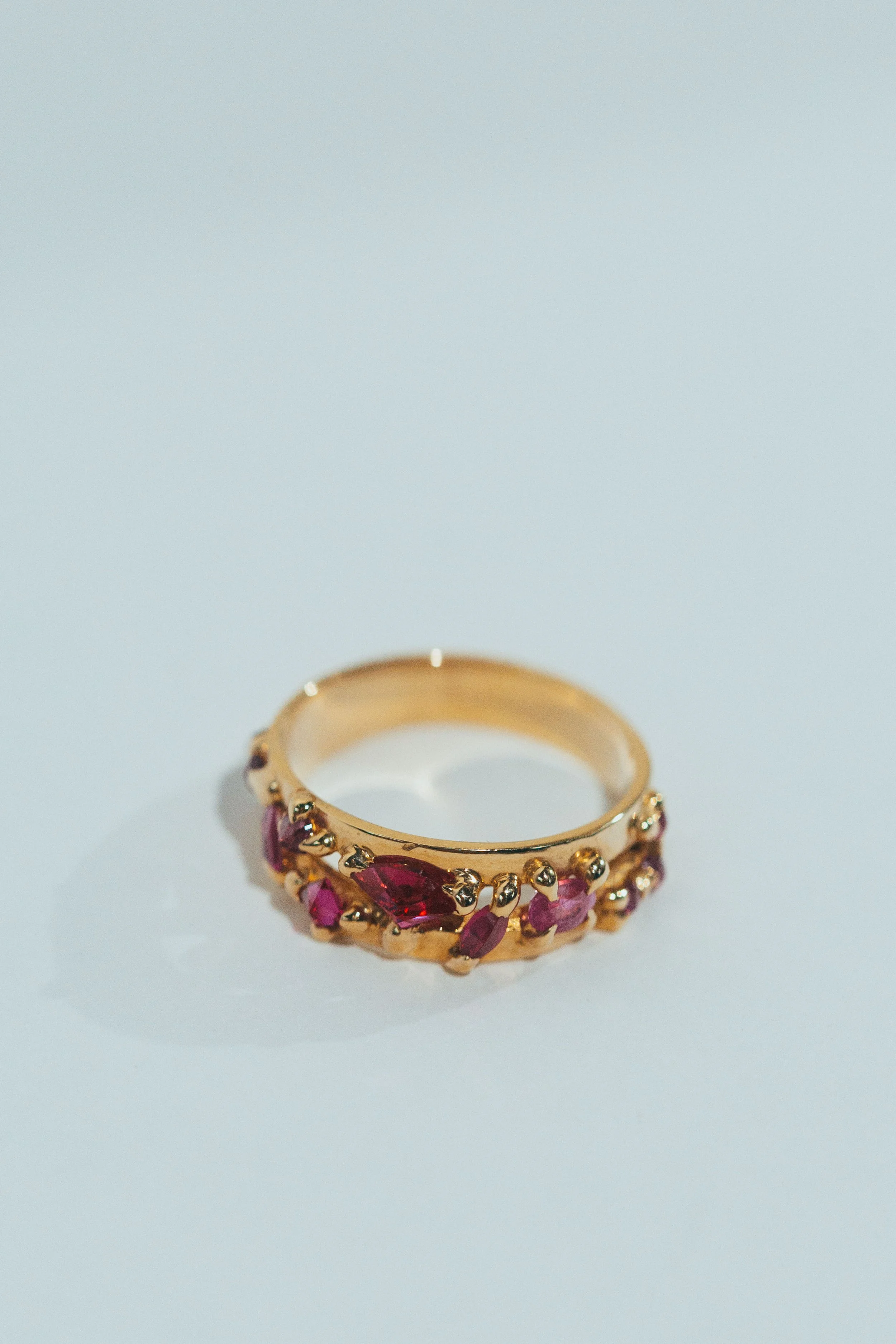 Gold ring with red and pink gemstones on a white surface.