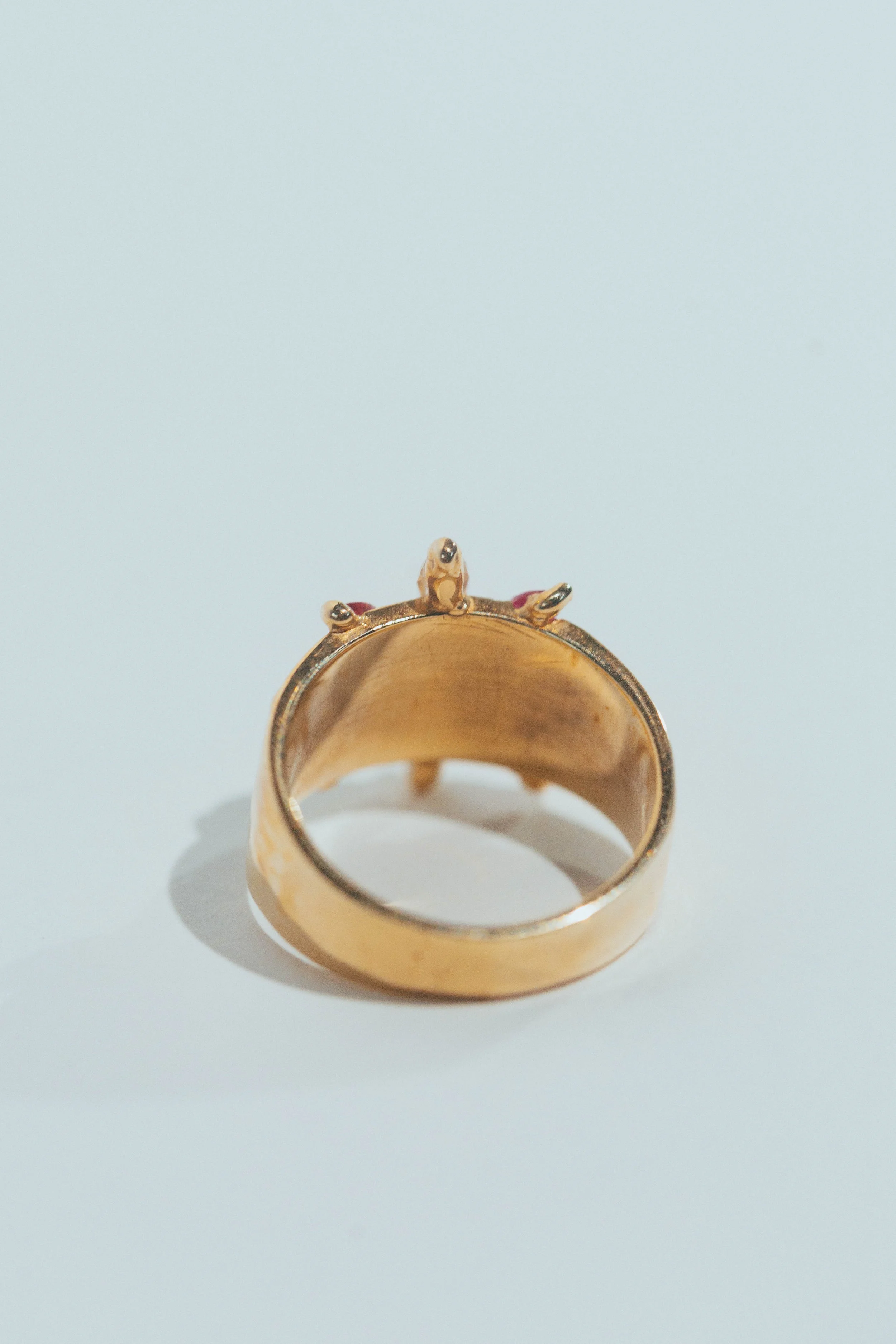 Gold ring with small frog design on top, placed on a white surface.