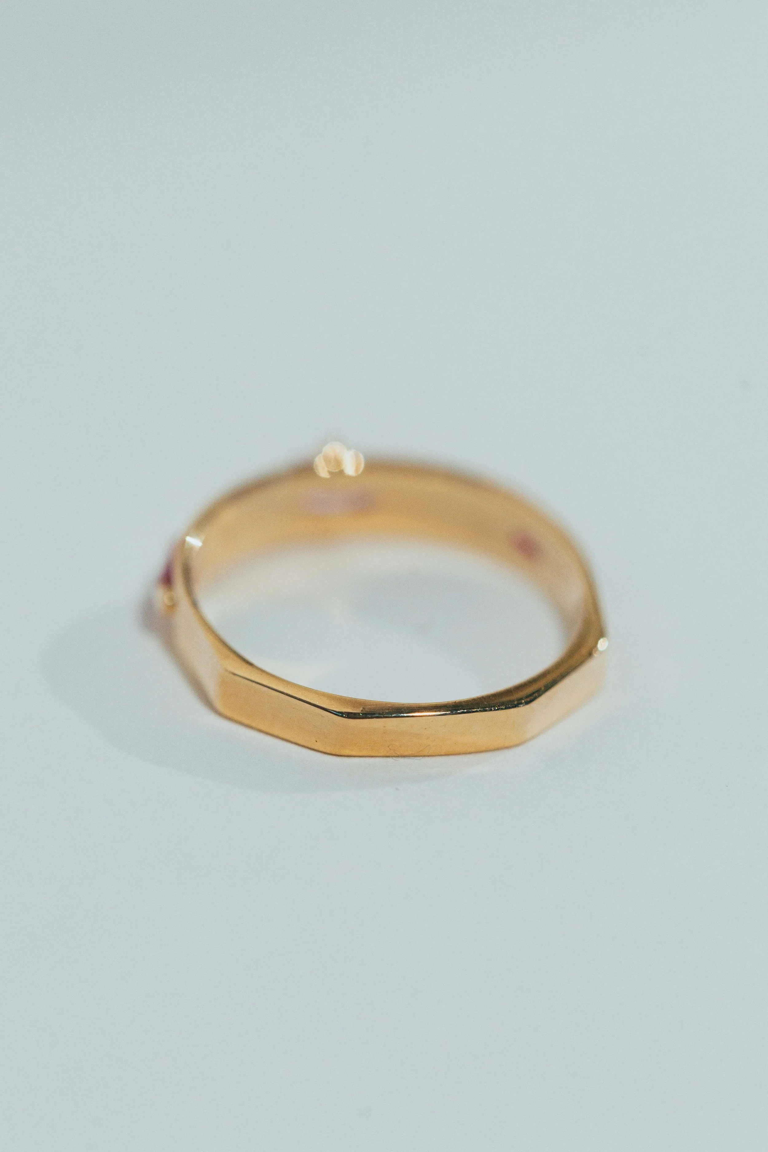 A gold ring with a faceted design, resting on a white surface.