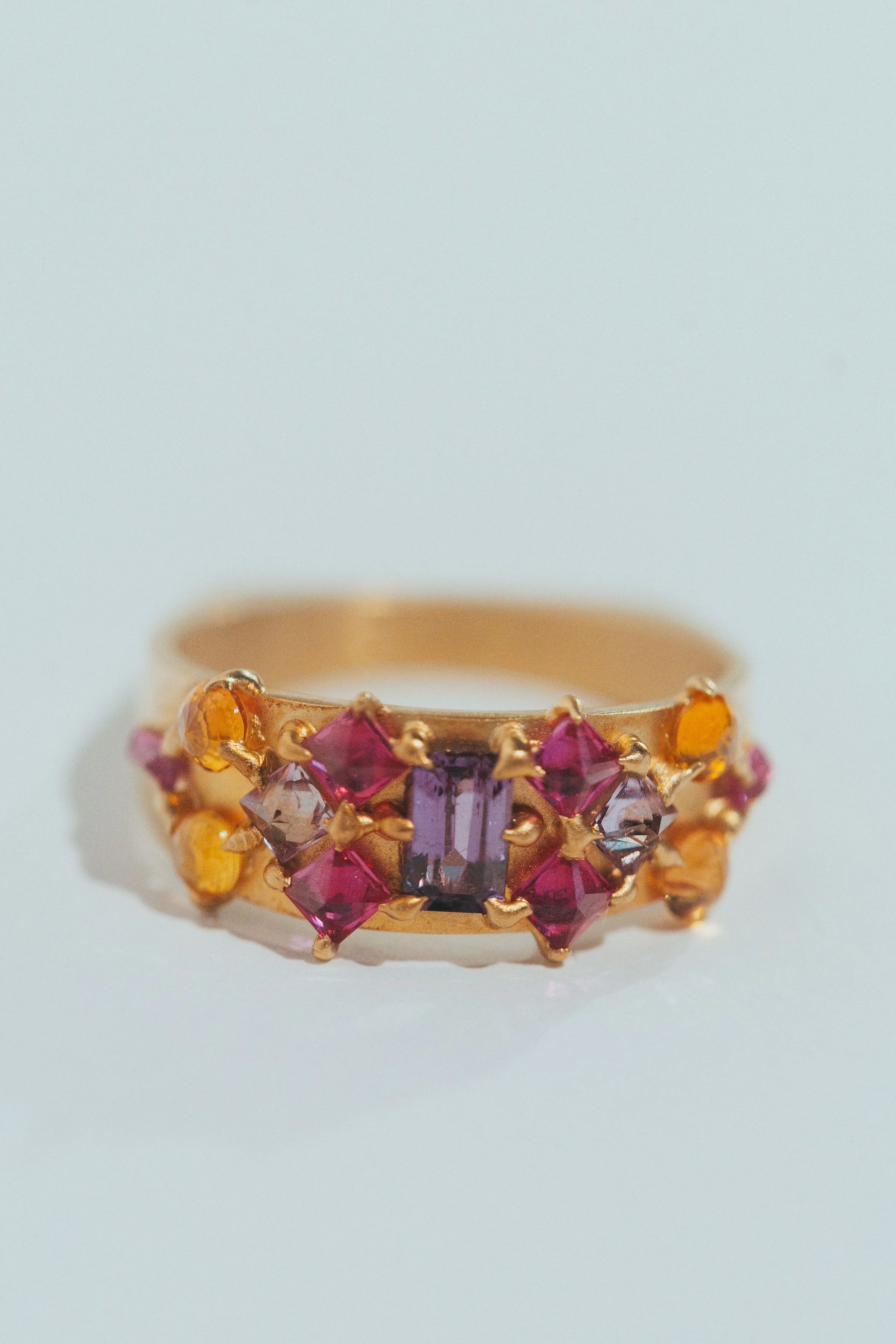 A bold 14kt yellow gold ring with square purple and pink sapphires around it. One-of-a-kind engagement rings. Inspired by ancient royalty.