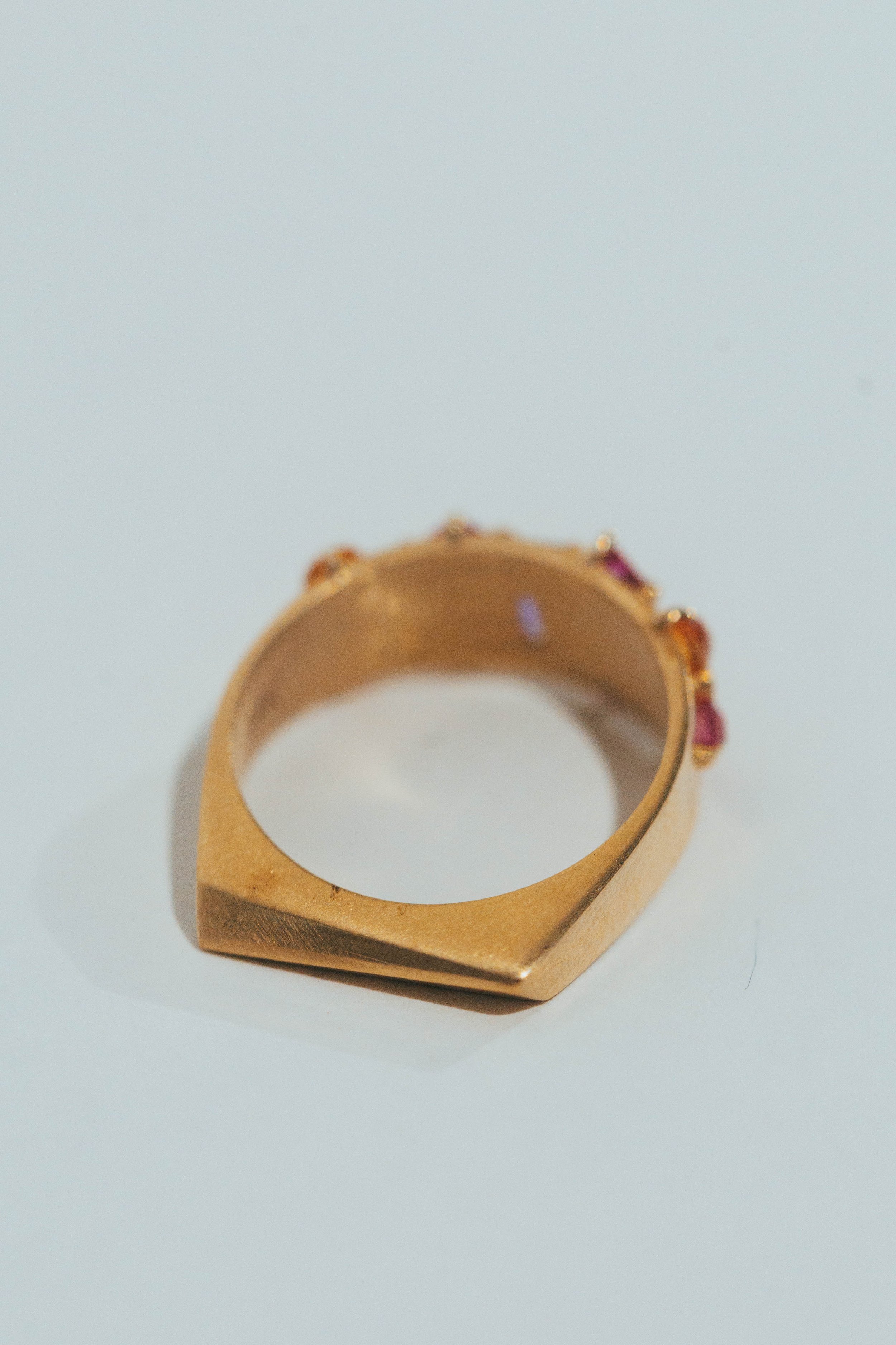 A gold ring with pink and purple gemstones on a white background.