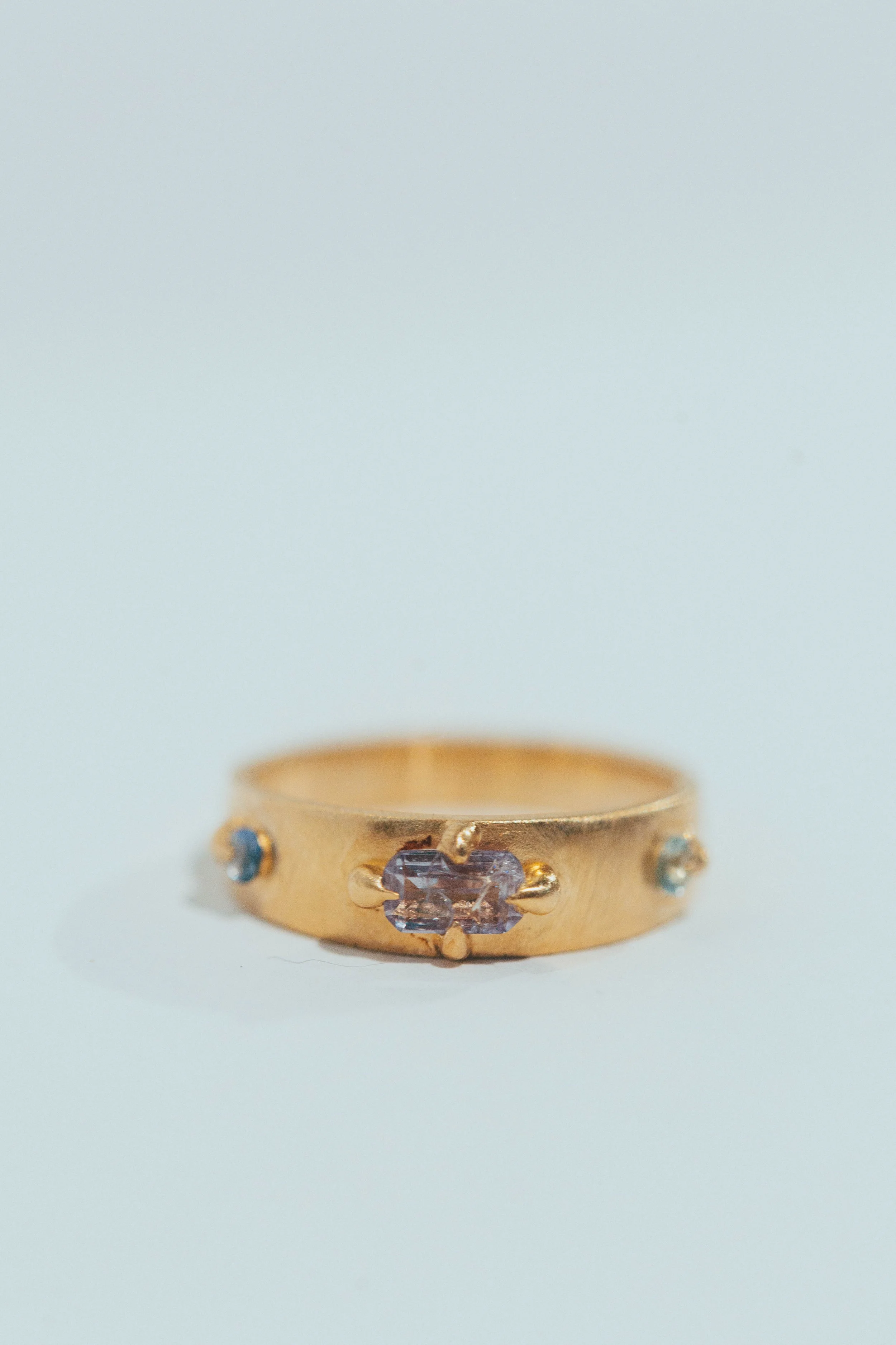 Gold ring with three small gemstones, centered on a white background.