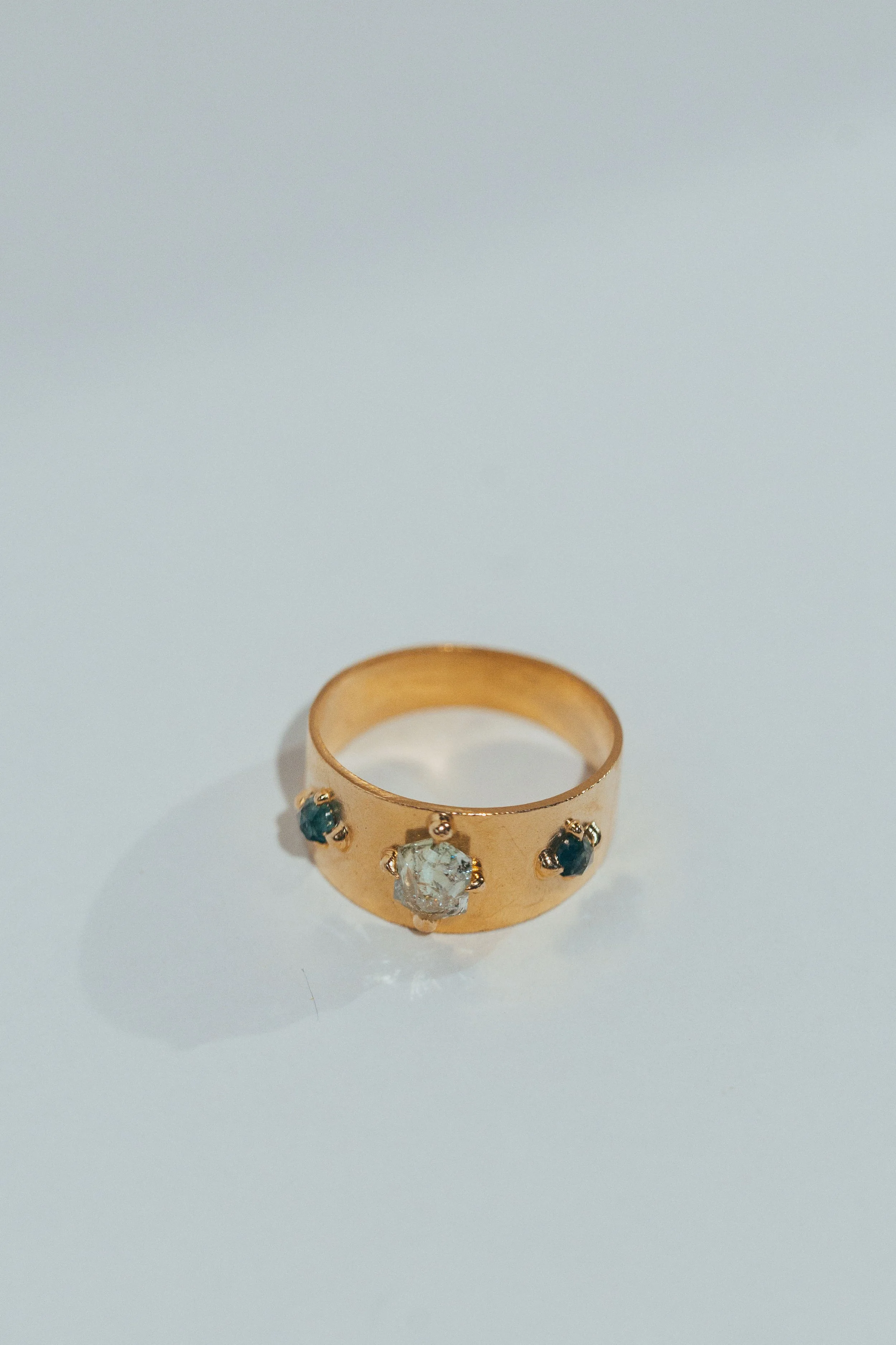 Gold ring with a large central gemstone and smaller blue gemstones on each side, on a white background.