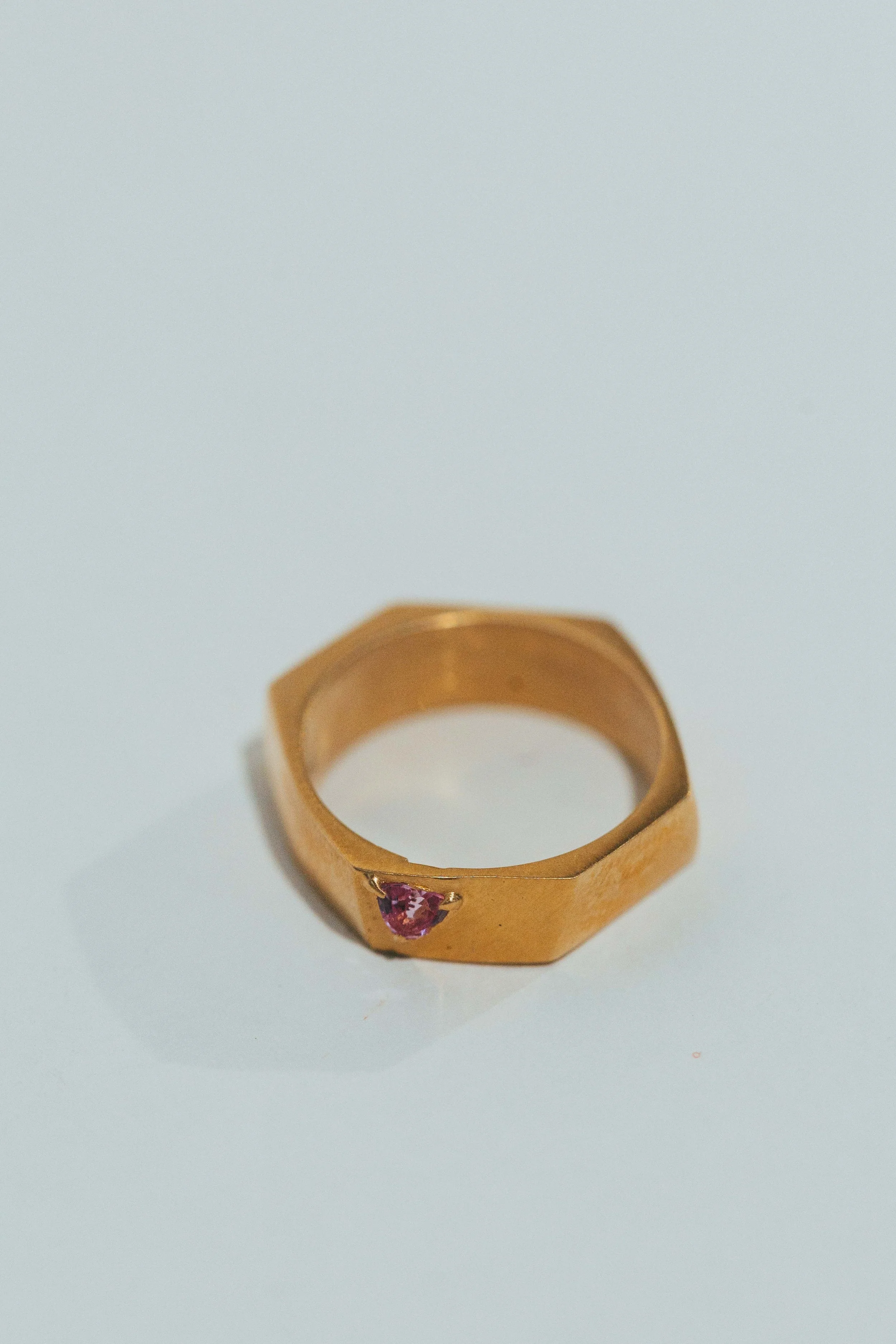 Gold ring with a pink gemstone on a light surface.