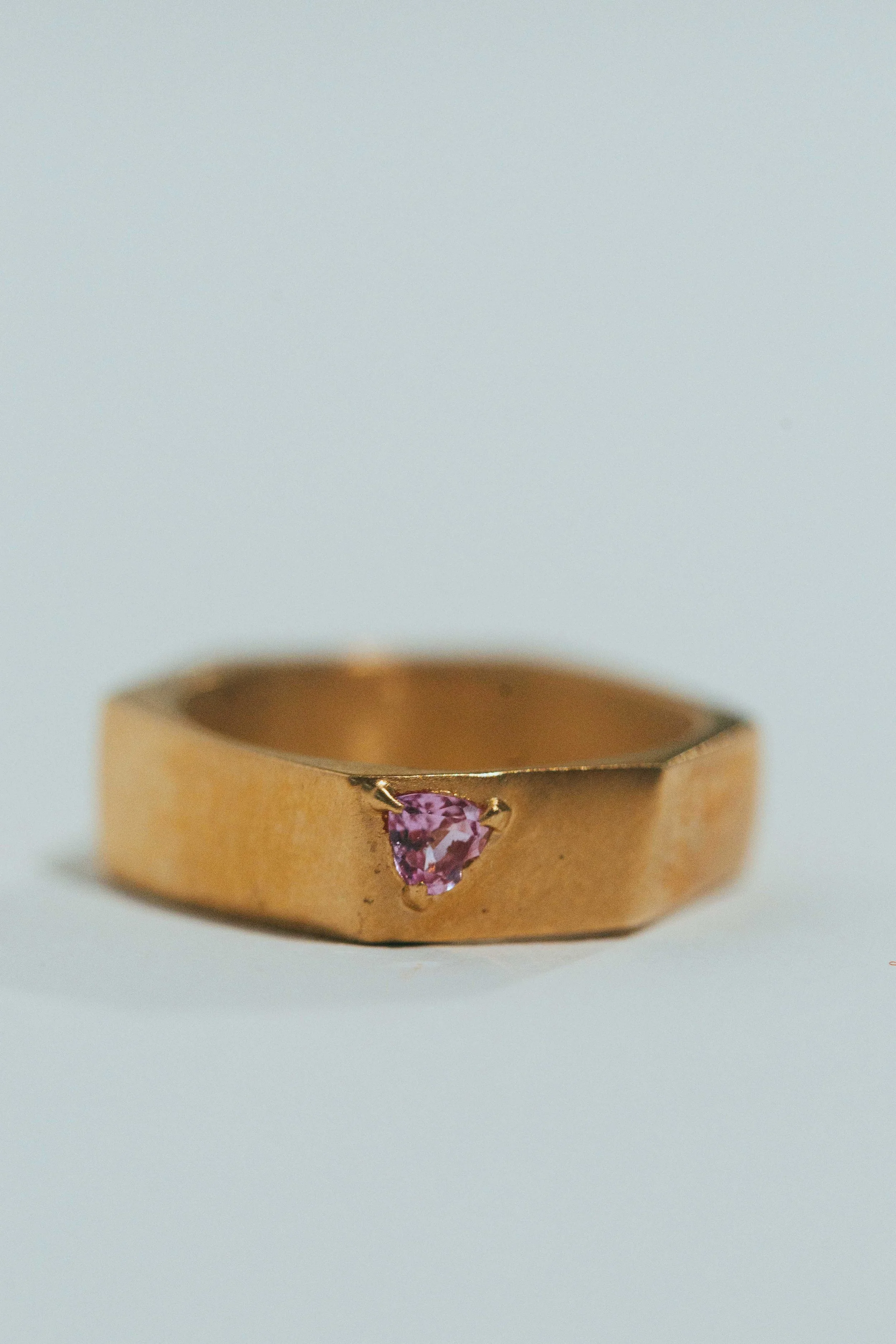Gold ring with a pink gemstone set in a triangle shape.
