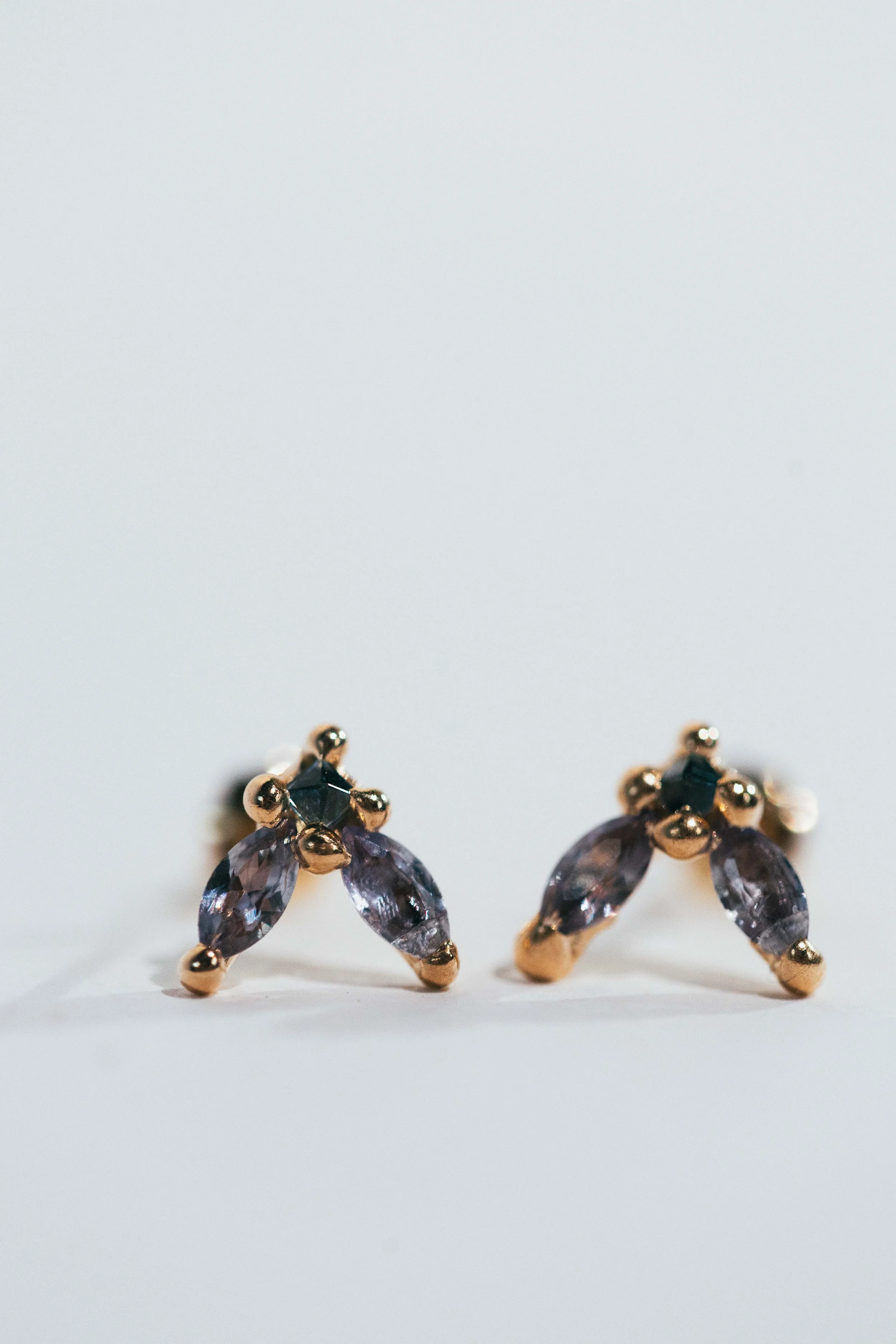 Pair of gold and purple gemstone earrings on a white background
