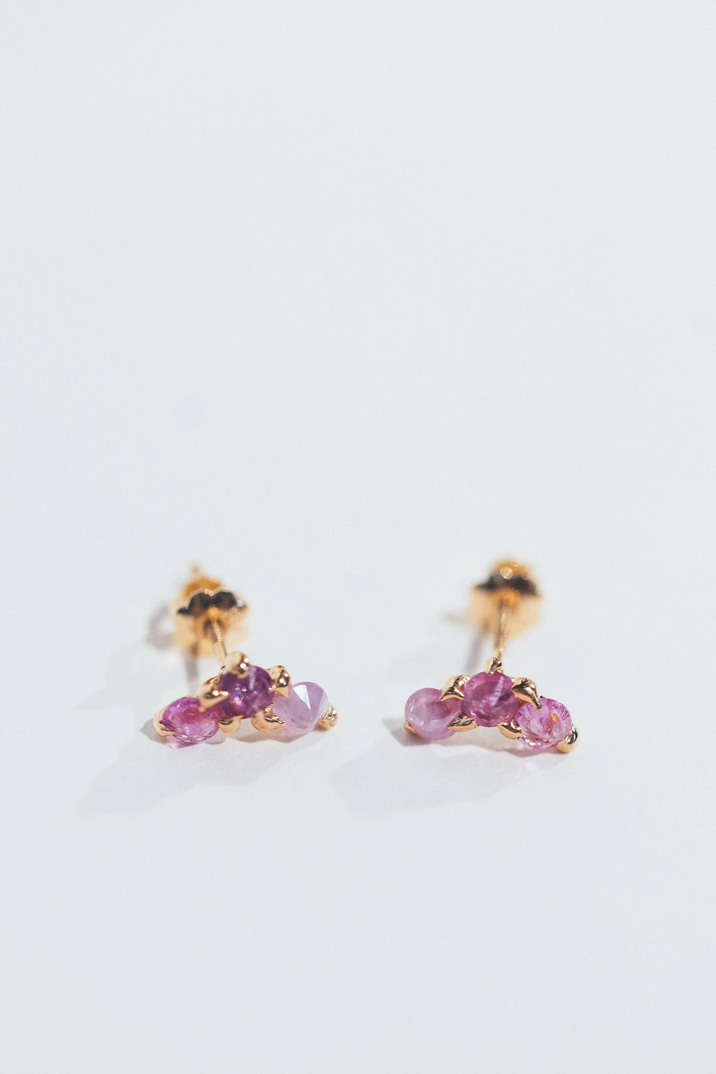 Pair of gold earrings with purple gemstones placed on a white surface.