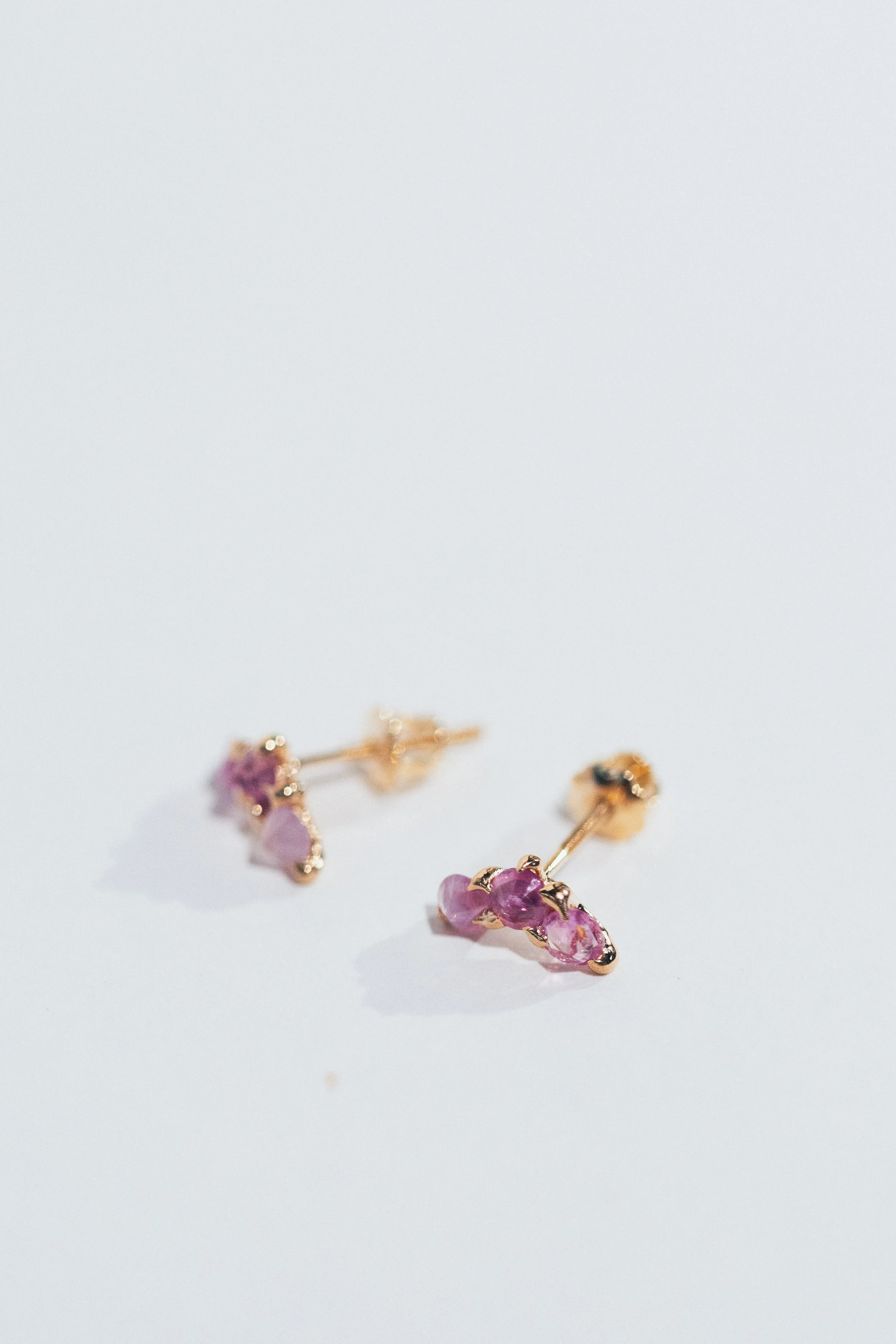 A pair of gold earrings with purple gemstones on a white surface.