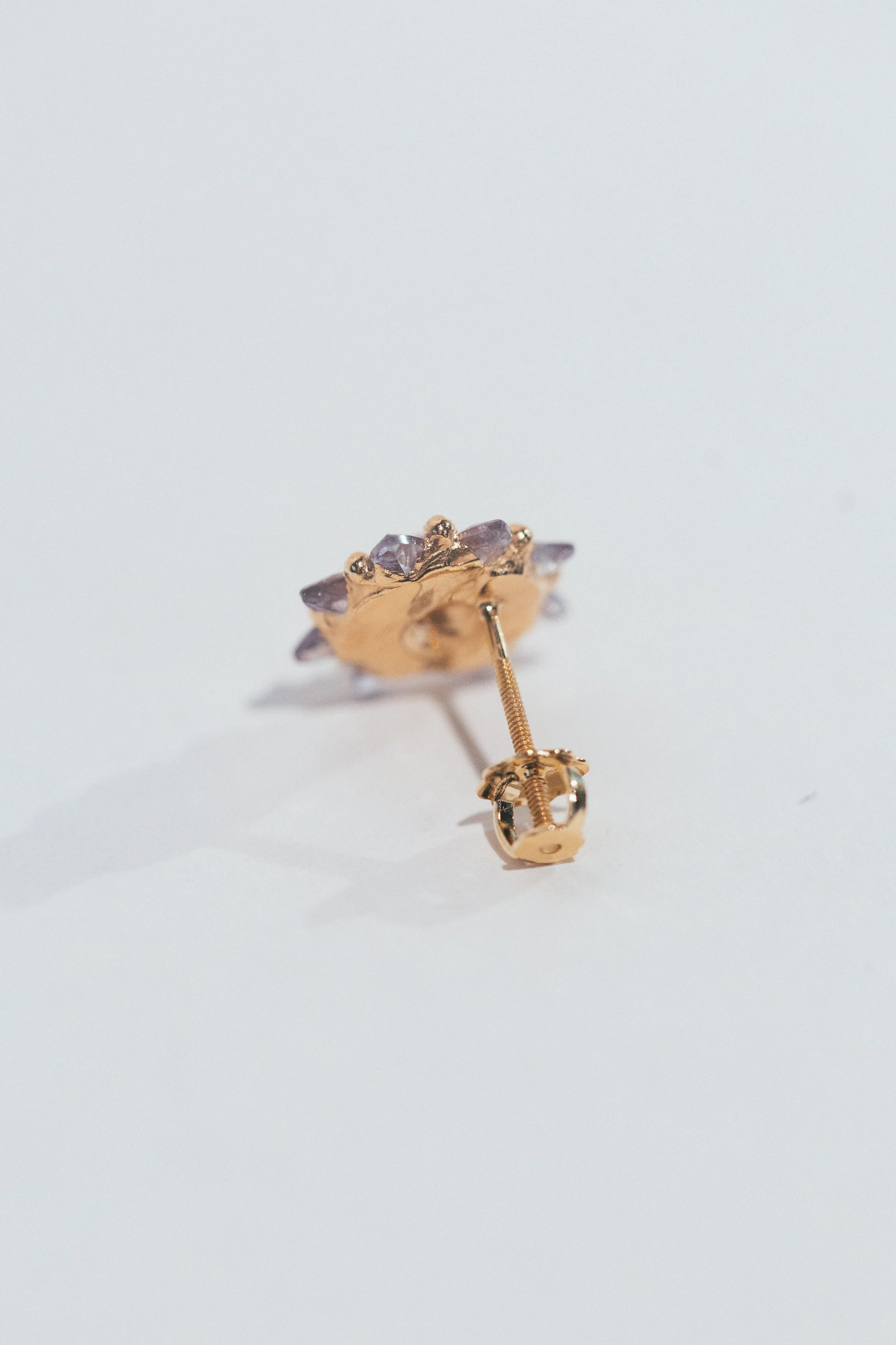 A gold and silver flower-shaped earring with purple gemstones, lying on a white surface.