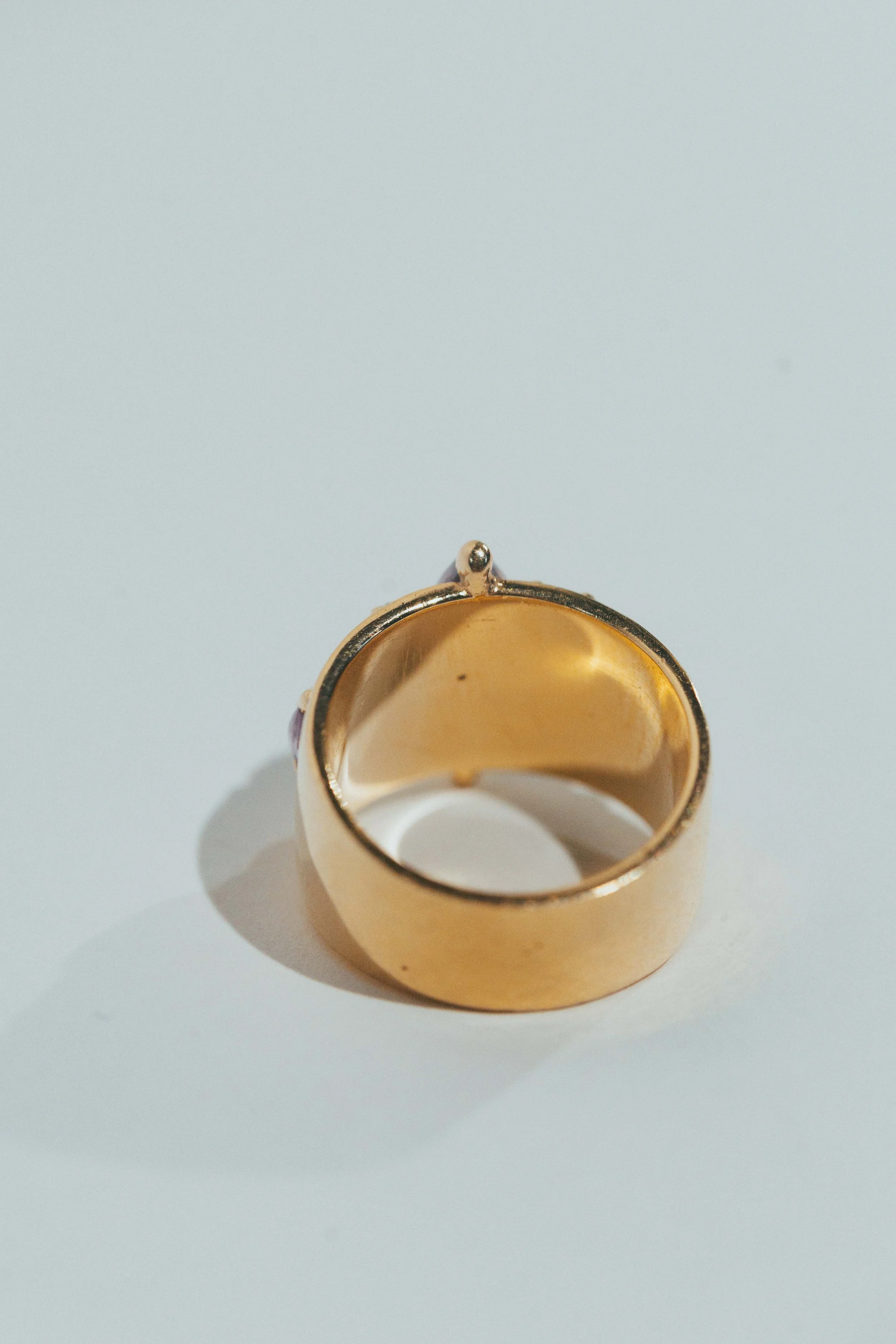 Close-up of a gold ring with an empty setting, lying on a white surface.