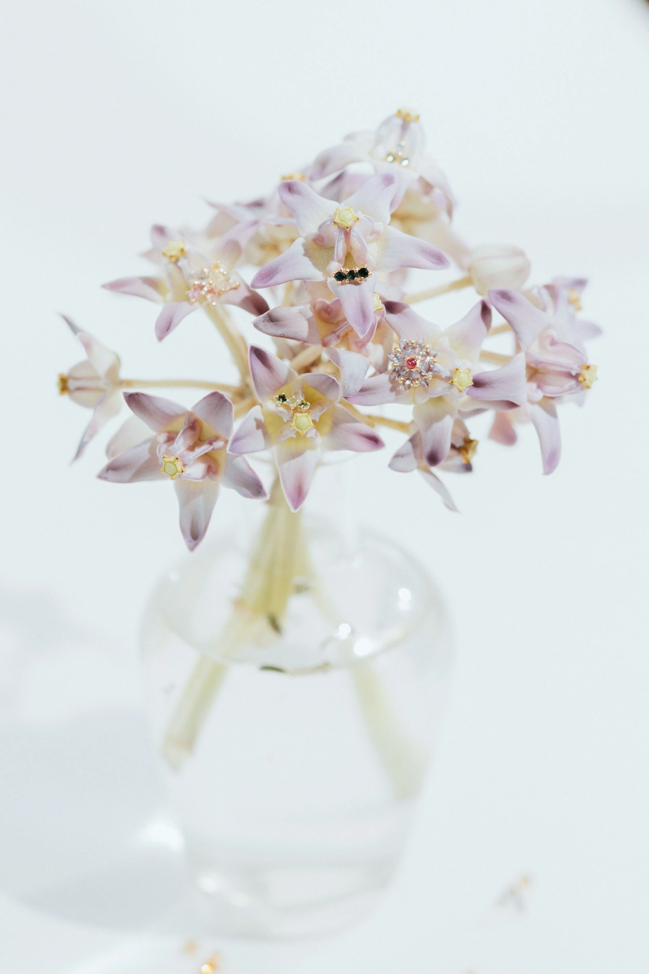 A clear glass vase holding a bouquet of pale pink and white hyacinth flowers, some decorated with jewelry.