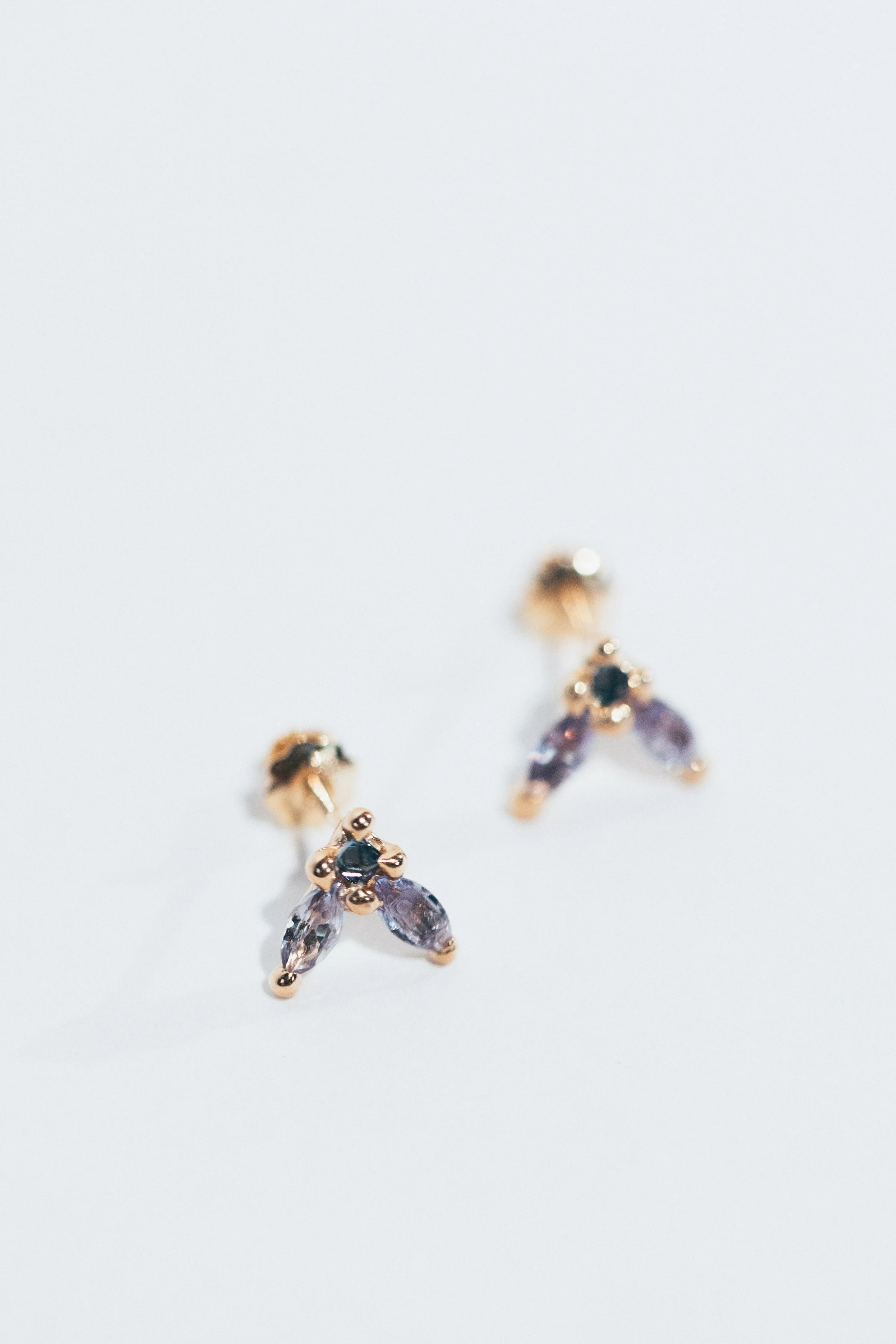 A pair of gold and purple gemstone earrings on a white background.