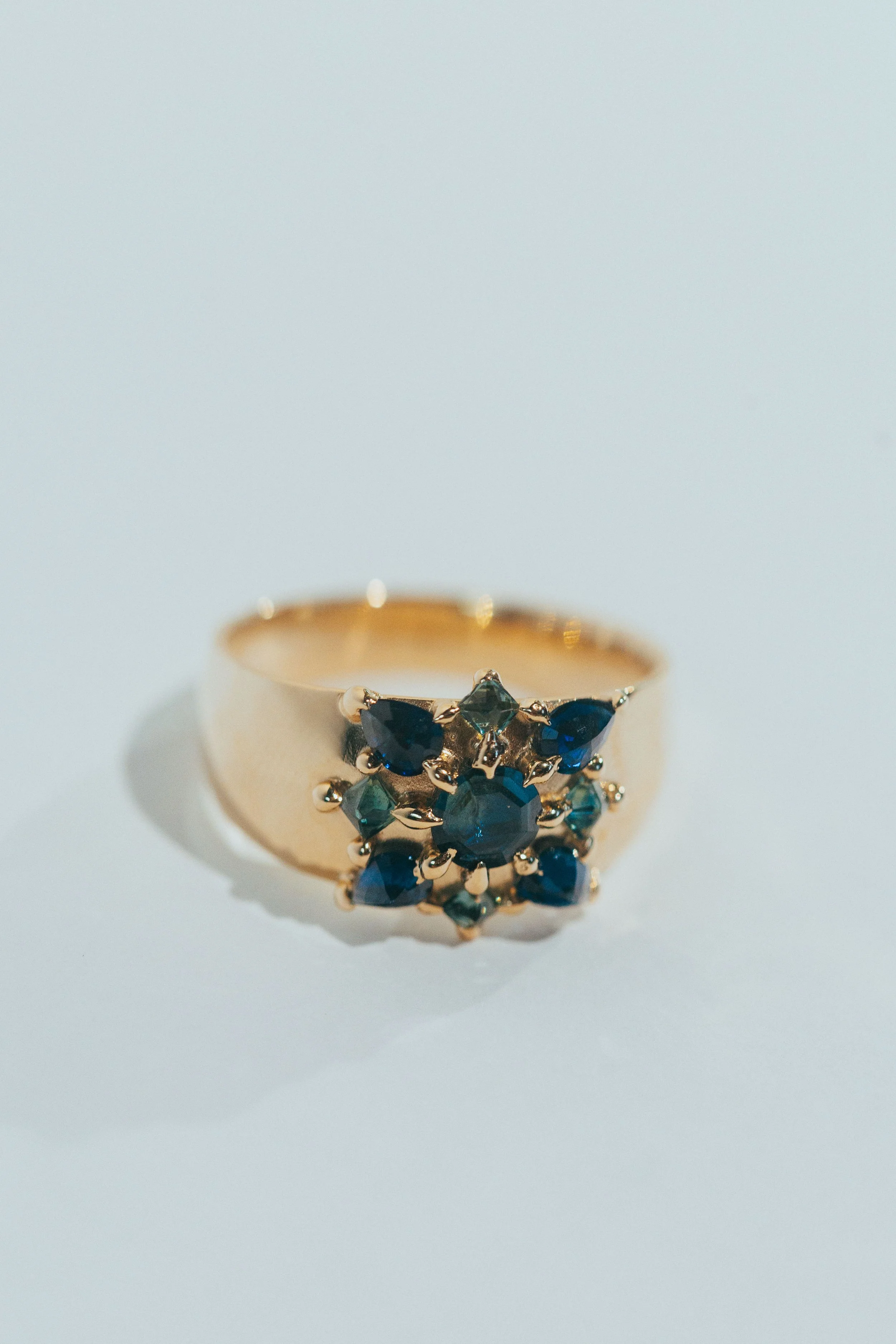 Gold ring with multiple small blue and green gemstones arranged in a floral pattern.