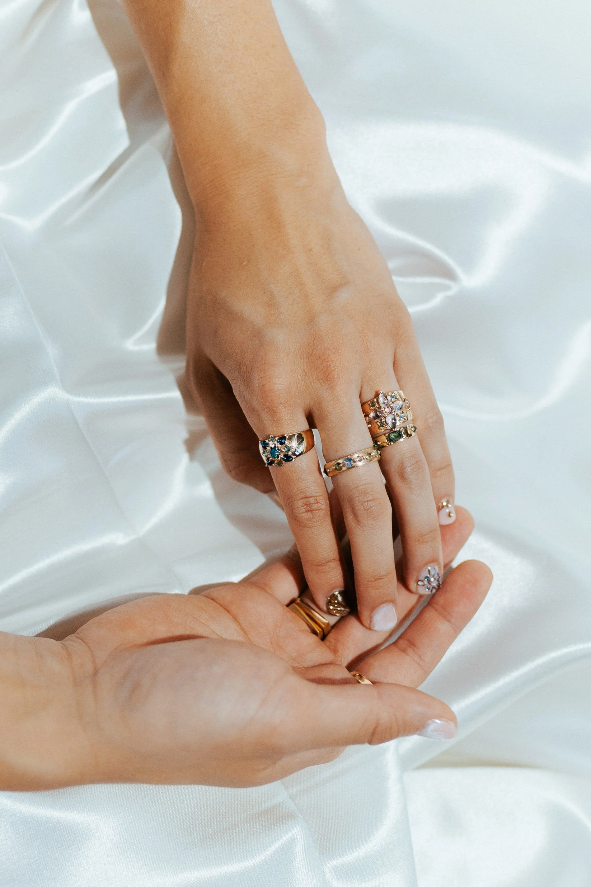 Close-up of a hand with multiple rings on fingers, resting on a white satin cloth.
