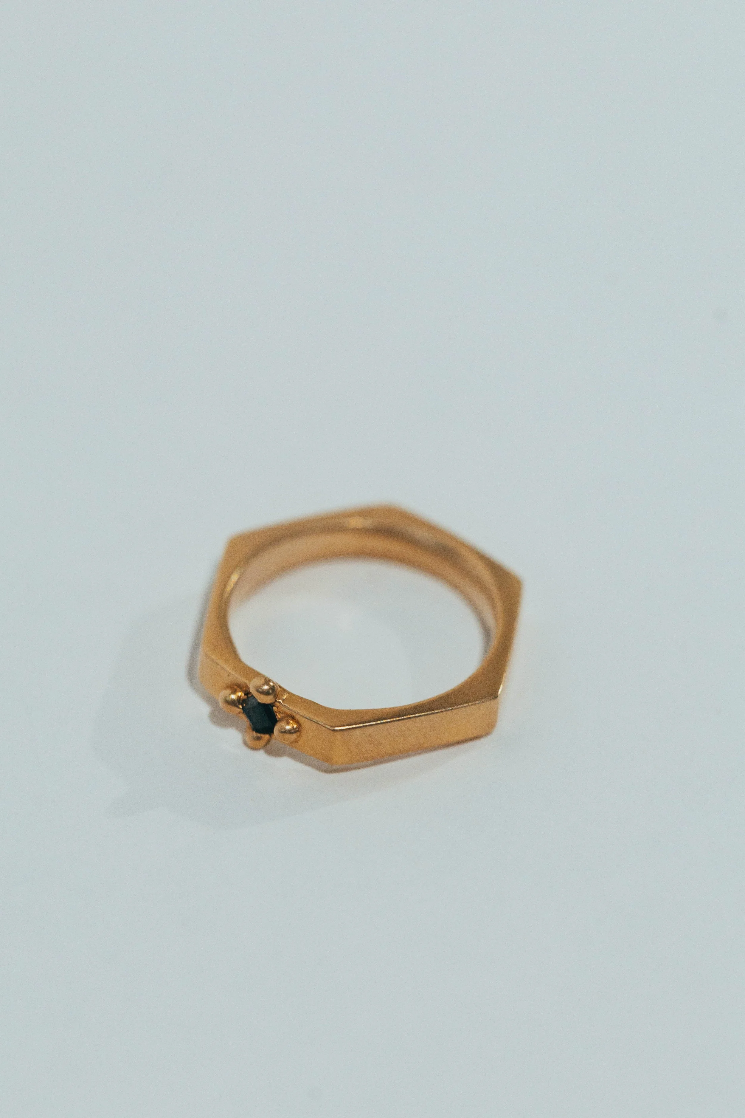 Gold geometric ring with black gemstone on a white surface.