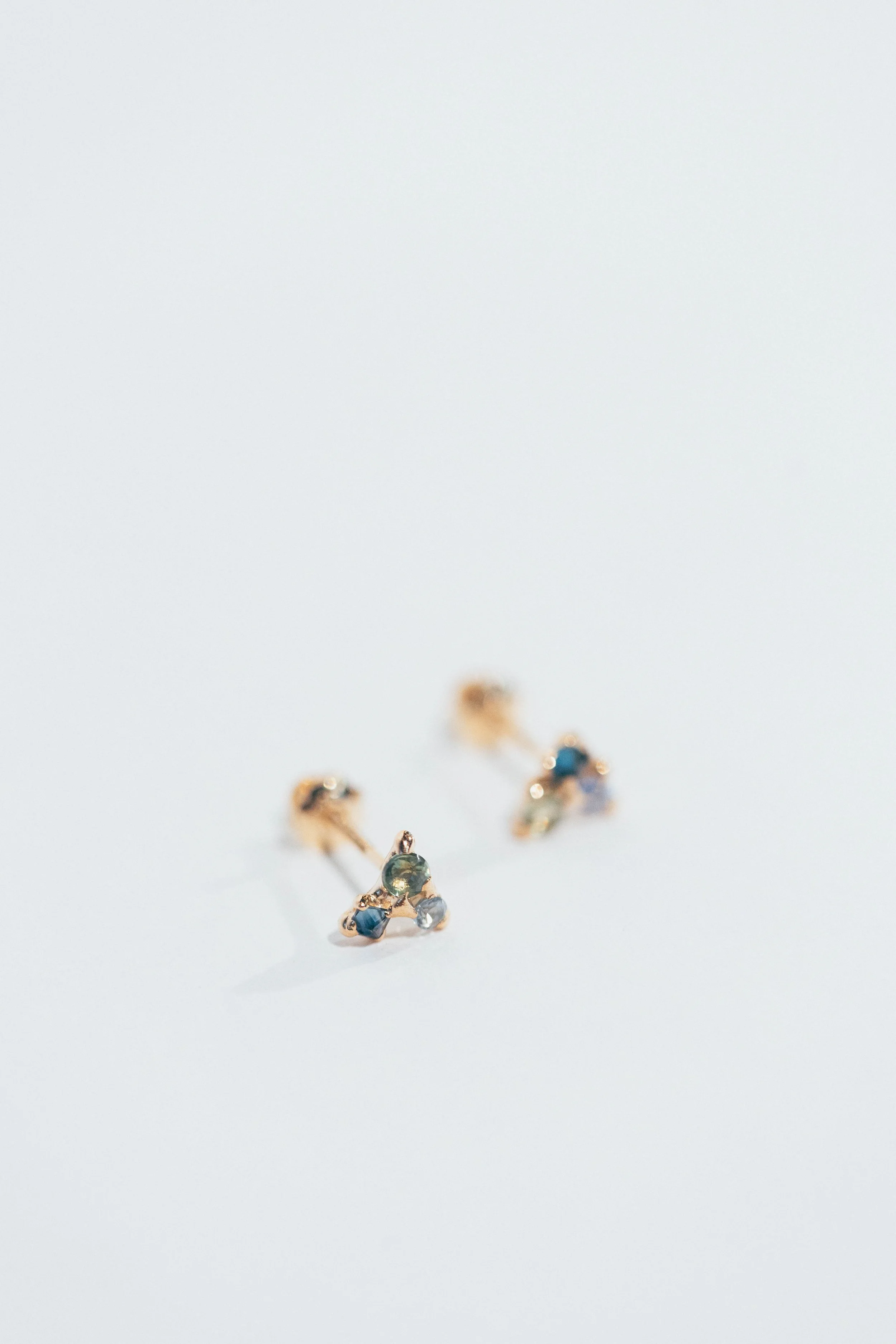 Pair of gold earrings with small blue and gray gemstones on a white background.