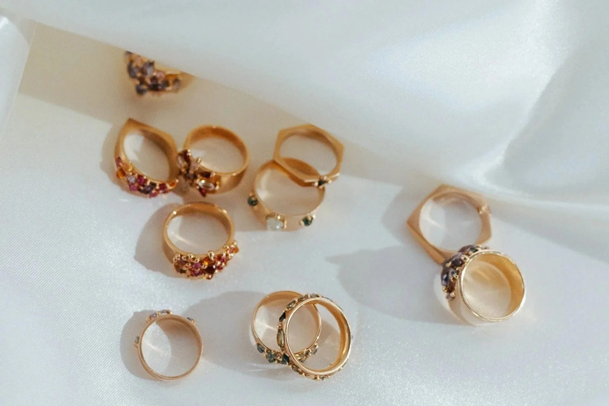 A collection of gold rings, some with colorful gemstones, arranged on white satin fabric.