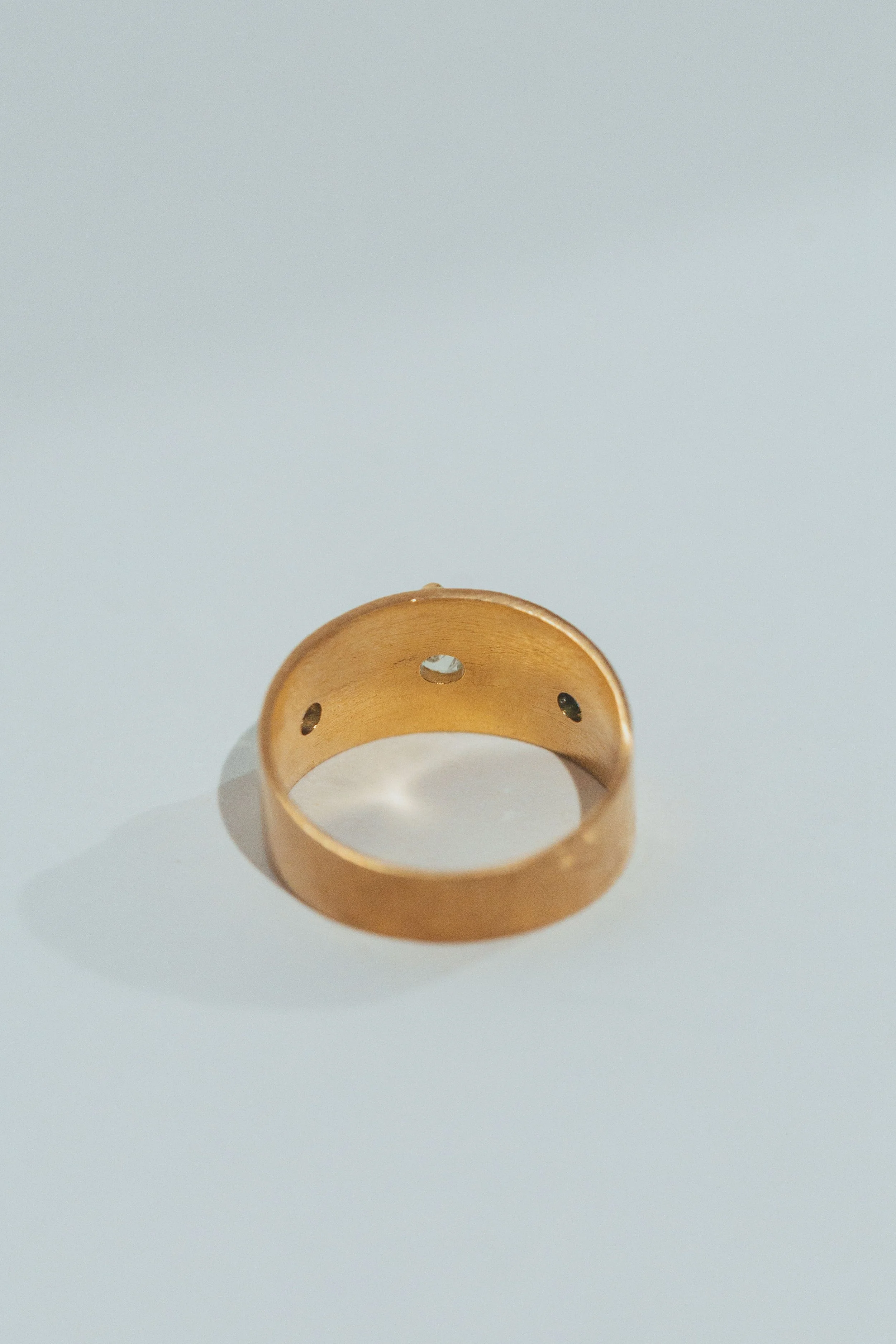 A gold ring with three small holes on the inner side, placed on a white surface.