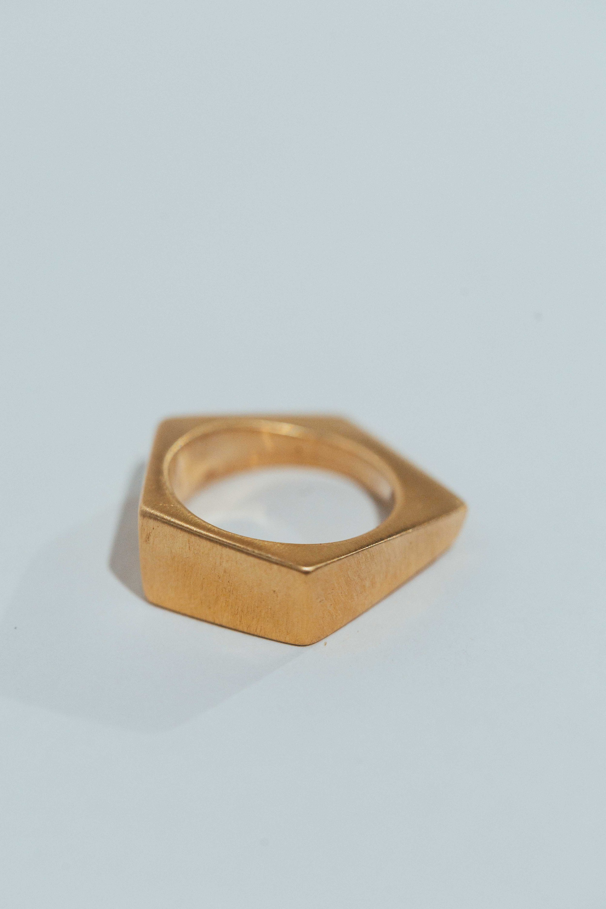 A gold ring with a square-shaped top and a circular hole in the center, placed on a white surface.