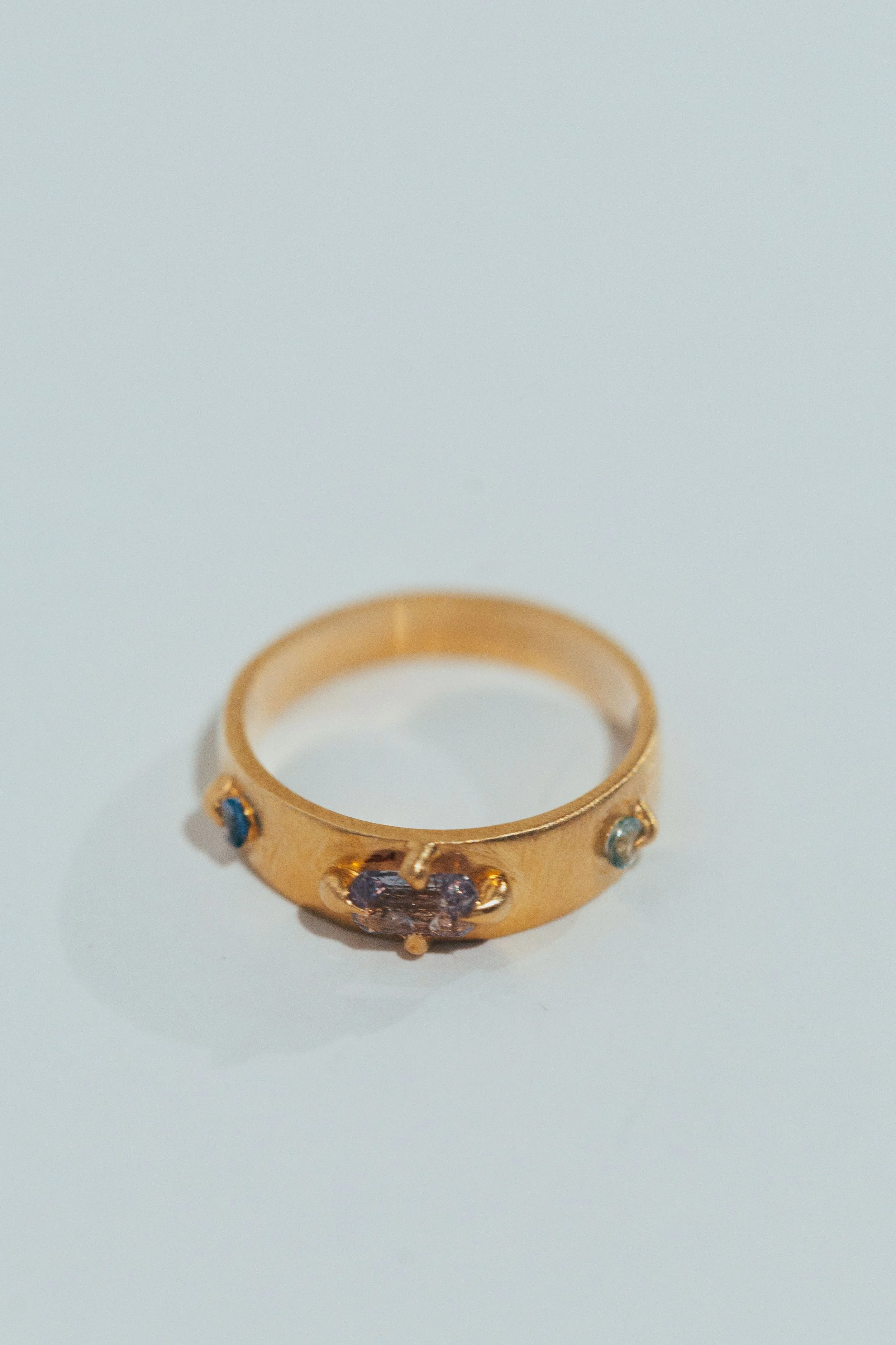 Gold ring with purple and blue gemstones on a white surface