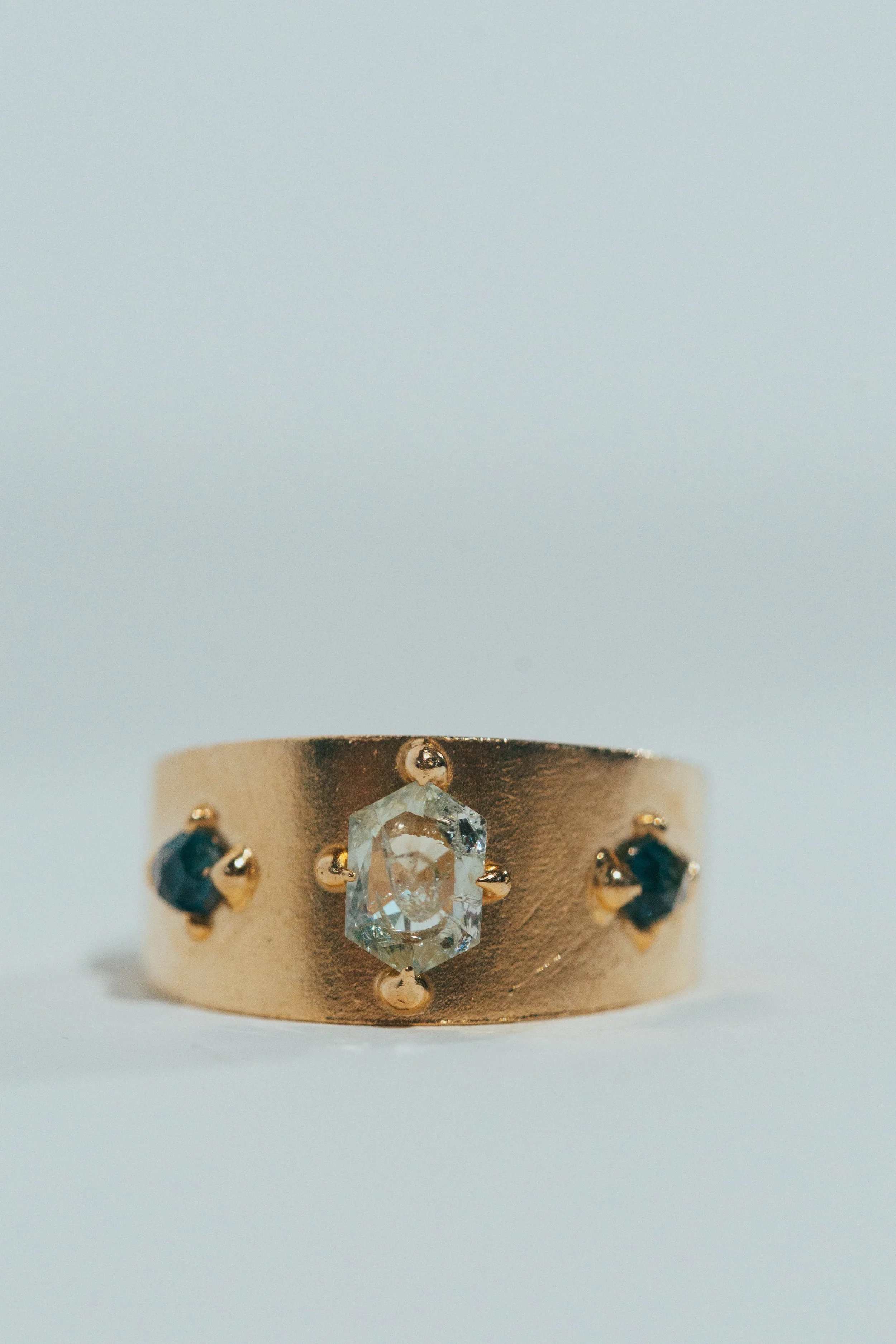 Close-up of a gold ring with a central rectangular diamond and two smaller blue sapphires on each side.