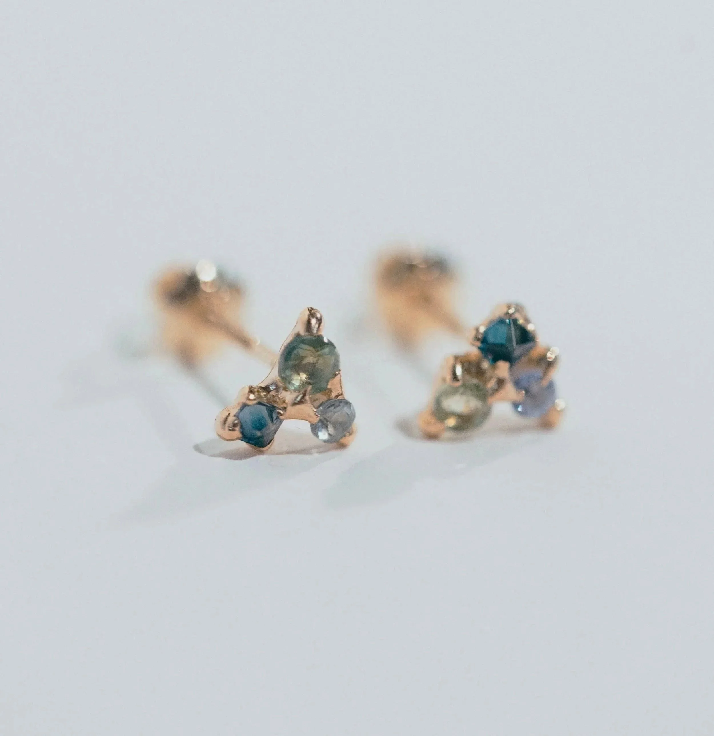 Close-up of a pair of gold earrings with small colorful gemstones on a white background.