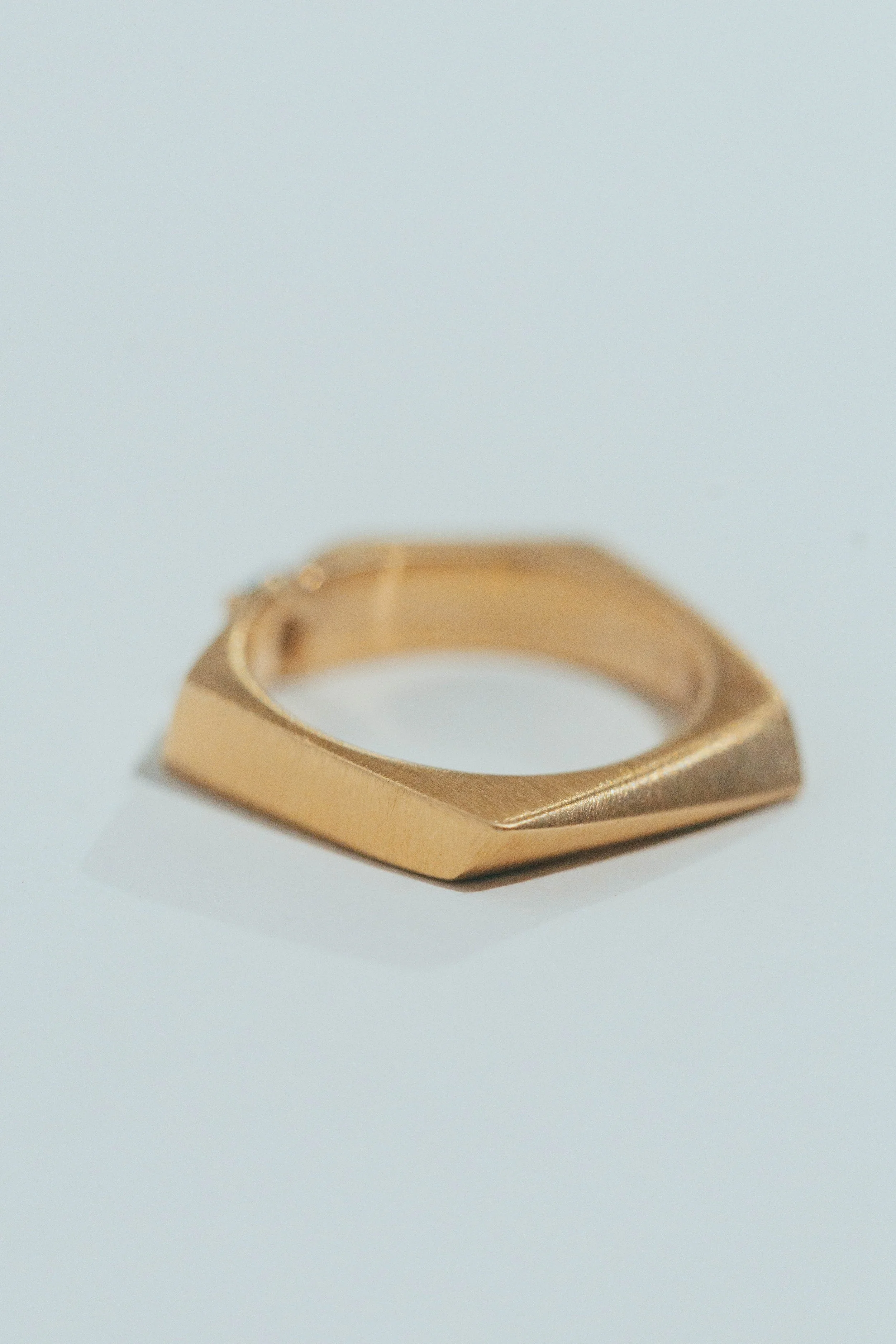 A gold ring with a geometric design on a white surface.