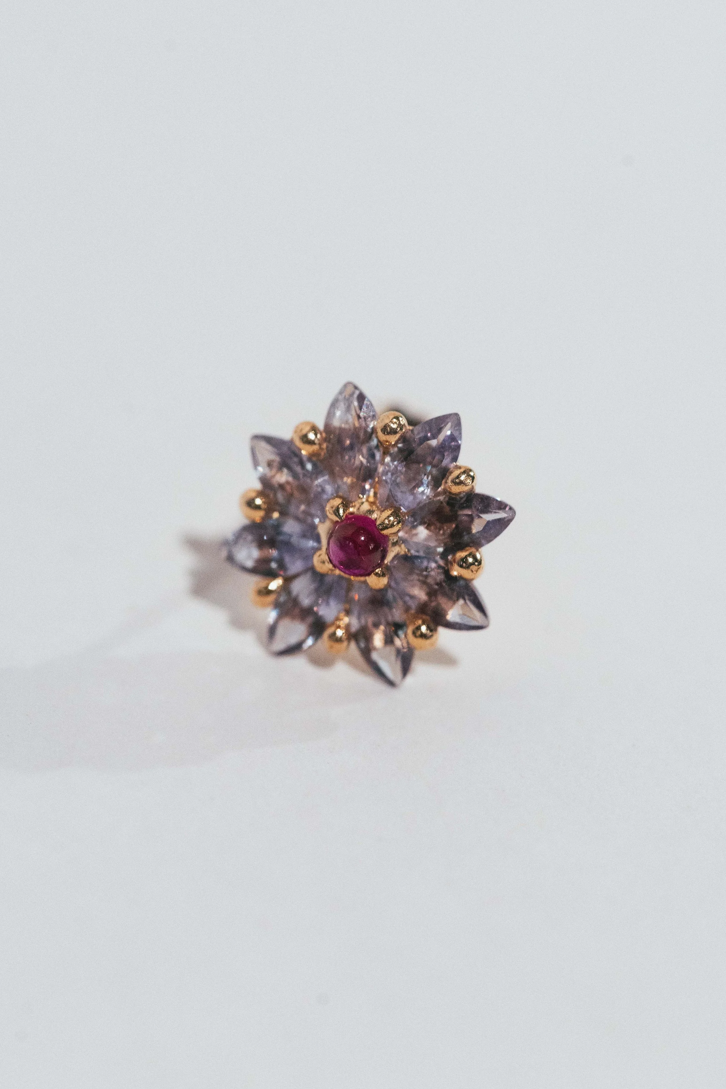 A floral-shaped ring with purple gemstones and a central red gemstone set in gold.