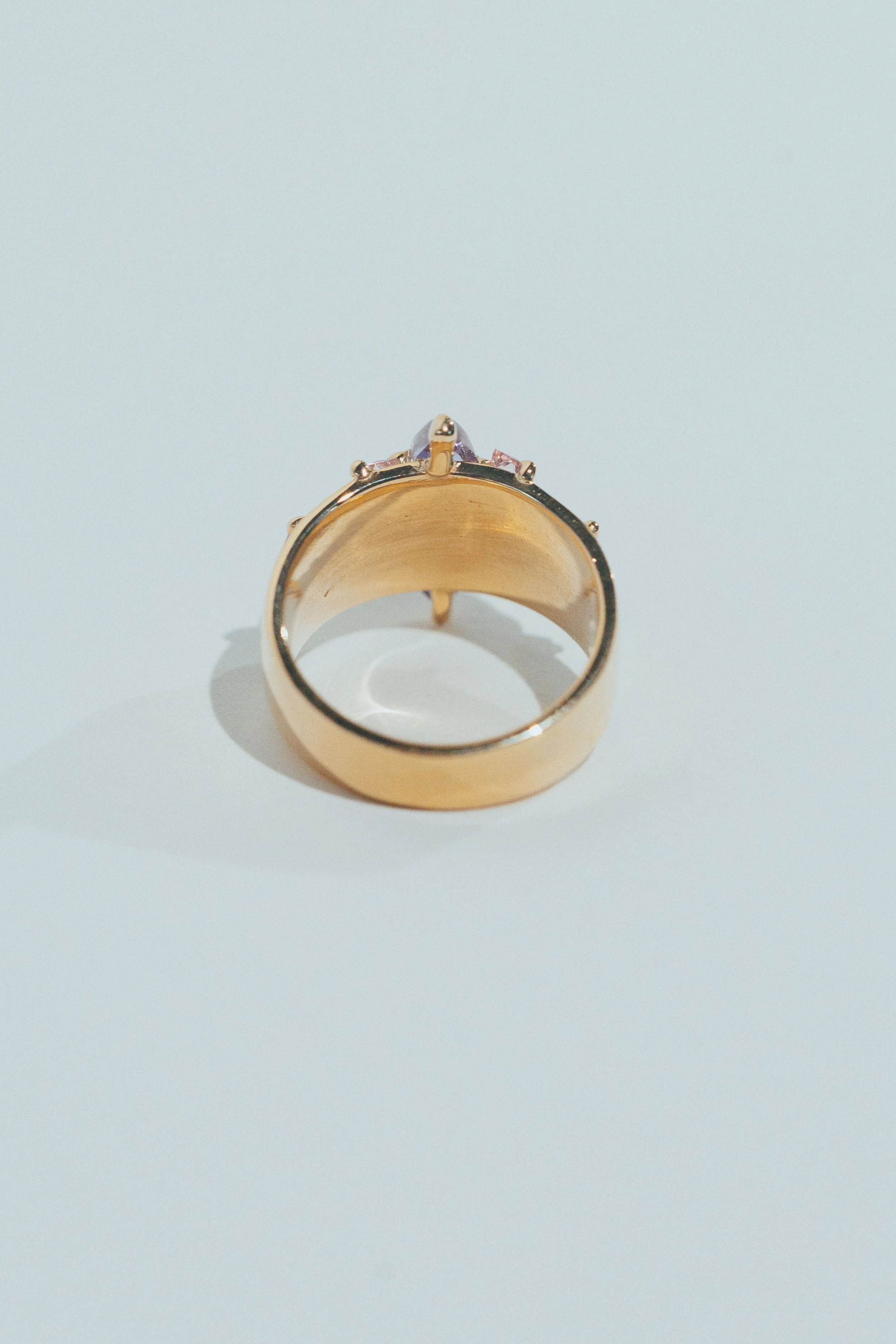 Gold ring with a purple gemstone viewed from above on a white surface.