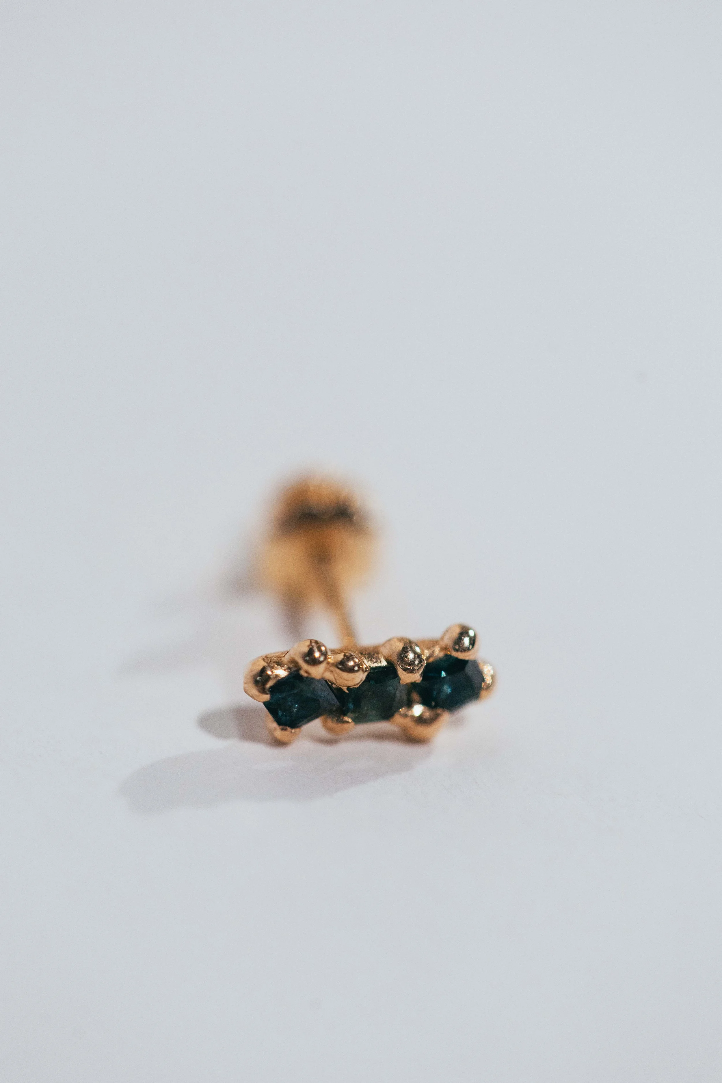 Close-up of a gold nose ring with black stones on a white background.