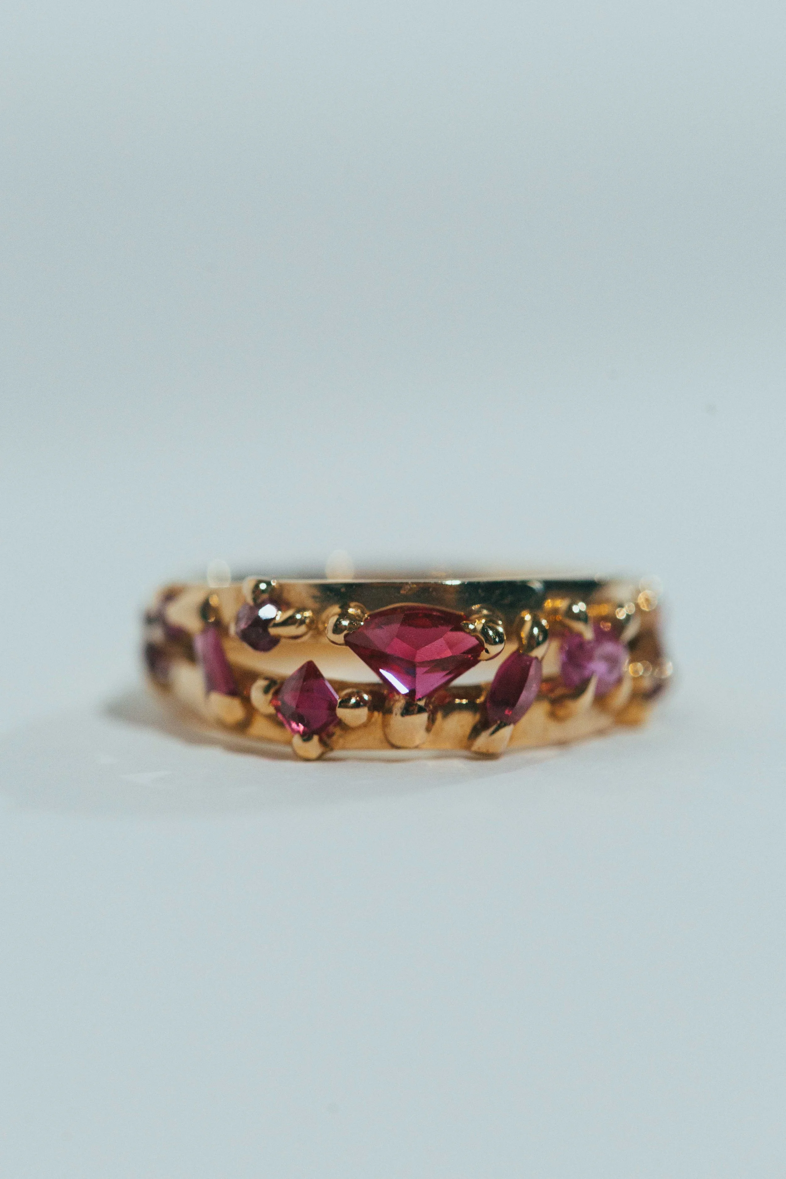 Gold ring with multiple pink gemstones, including a central heart-shaped stone, on a white background.