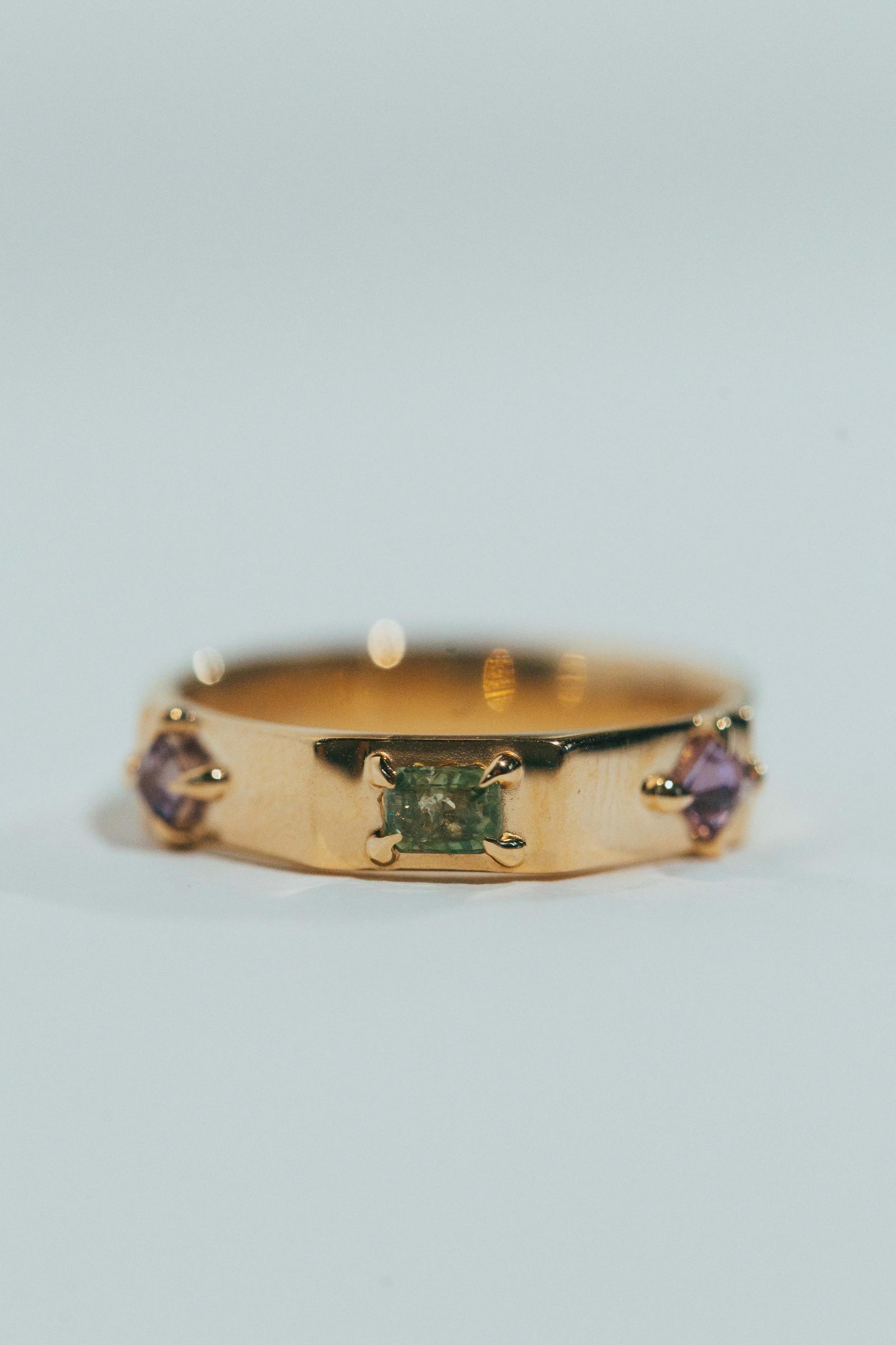 A gold ring with three gemstones, one in the center and two on the sides, on a white background.