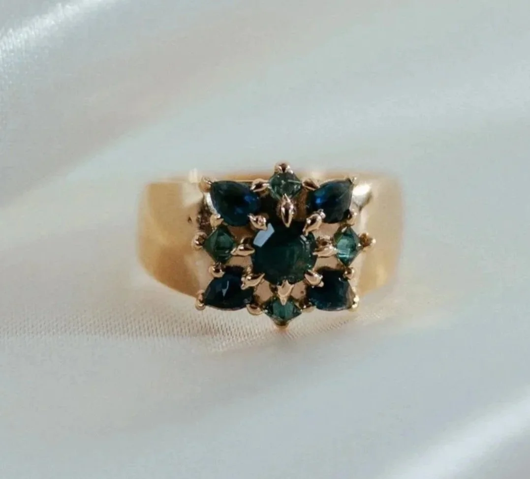 Gold ring with a cluster of dark green and blue gemstones in a floral pattern.