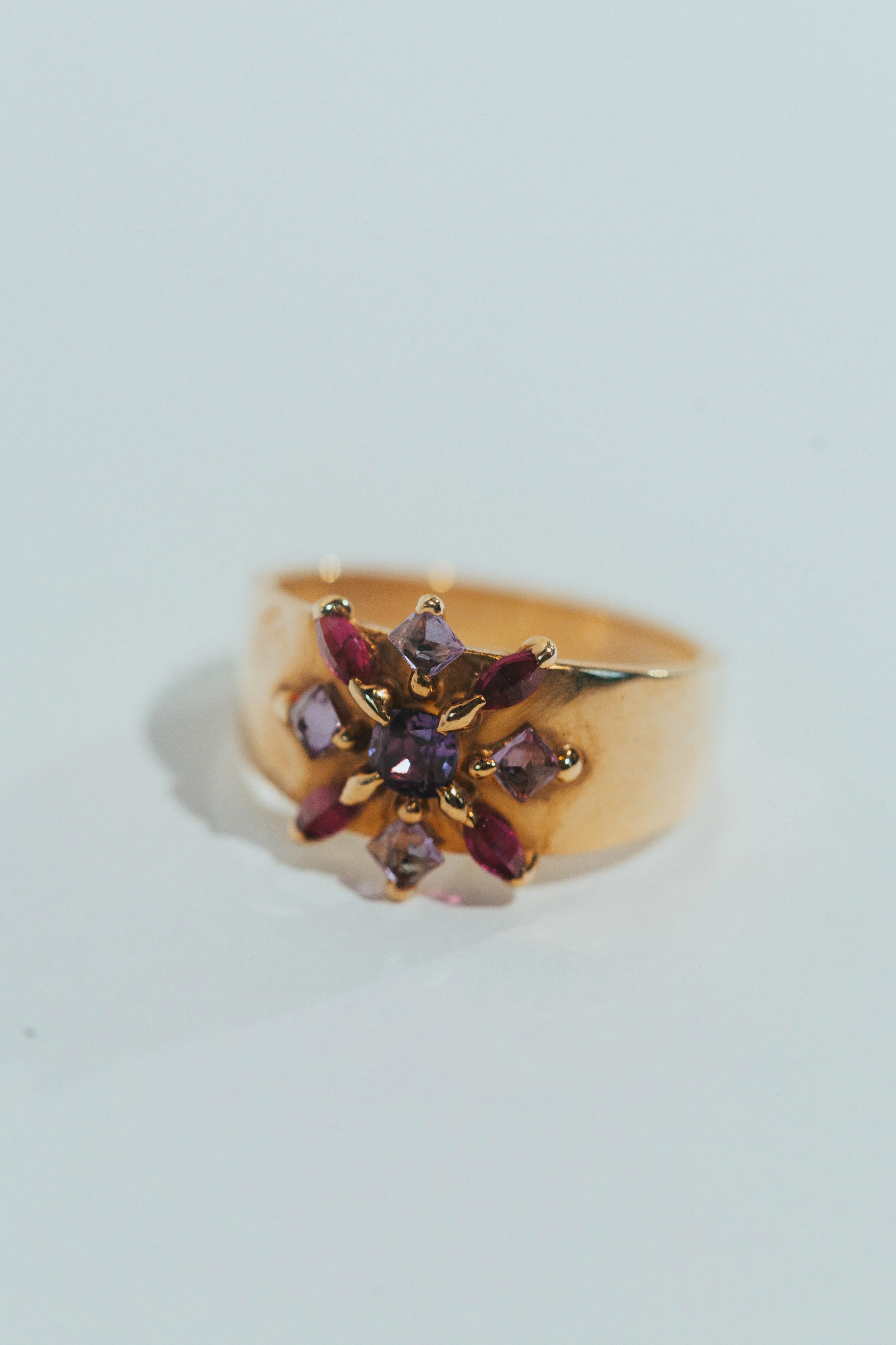 A gold ring with purple and pink gemstones arranged in a floral pattern.