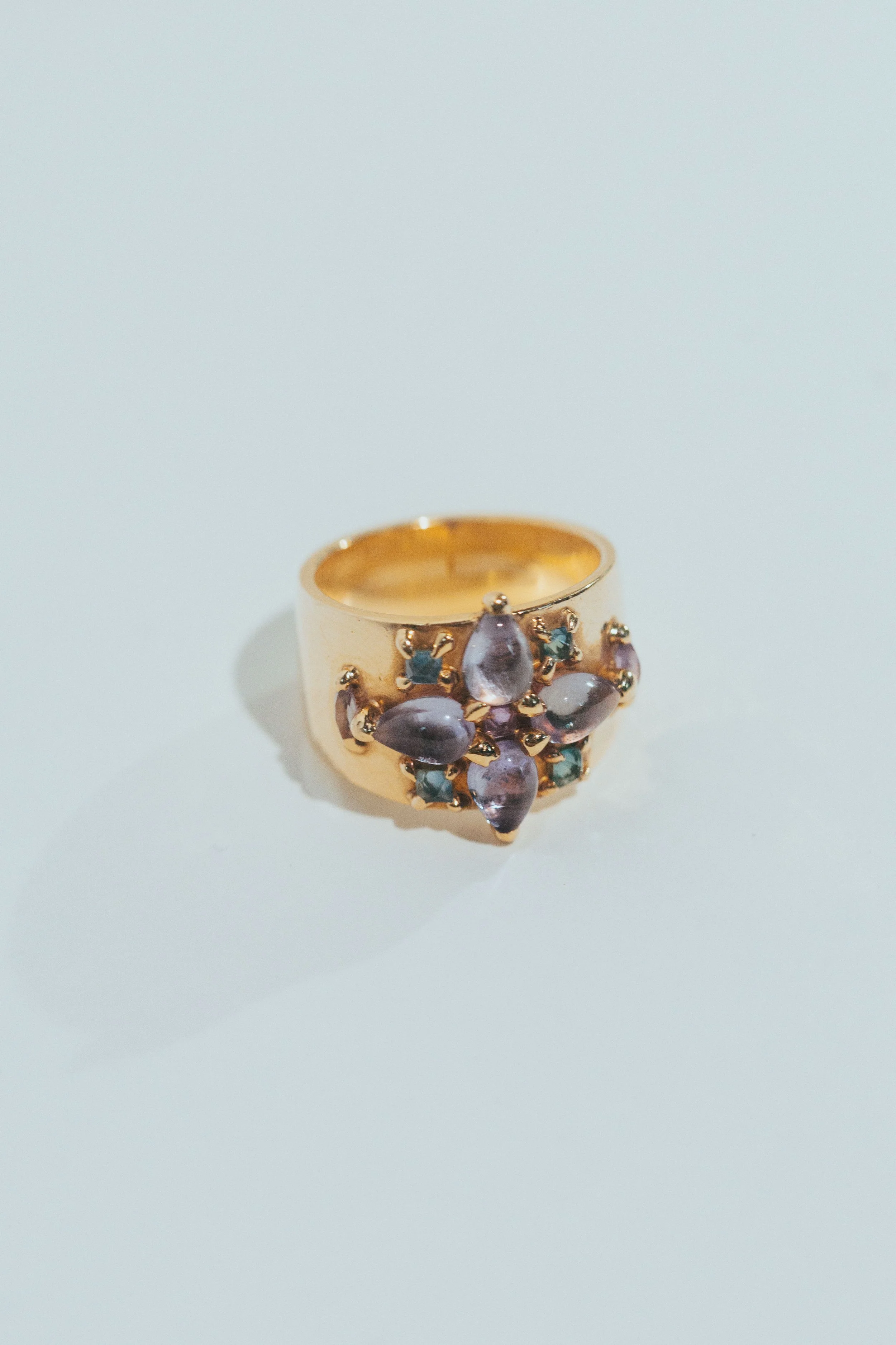 Gold ring with purple and green gemstones on a light background.